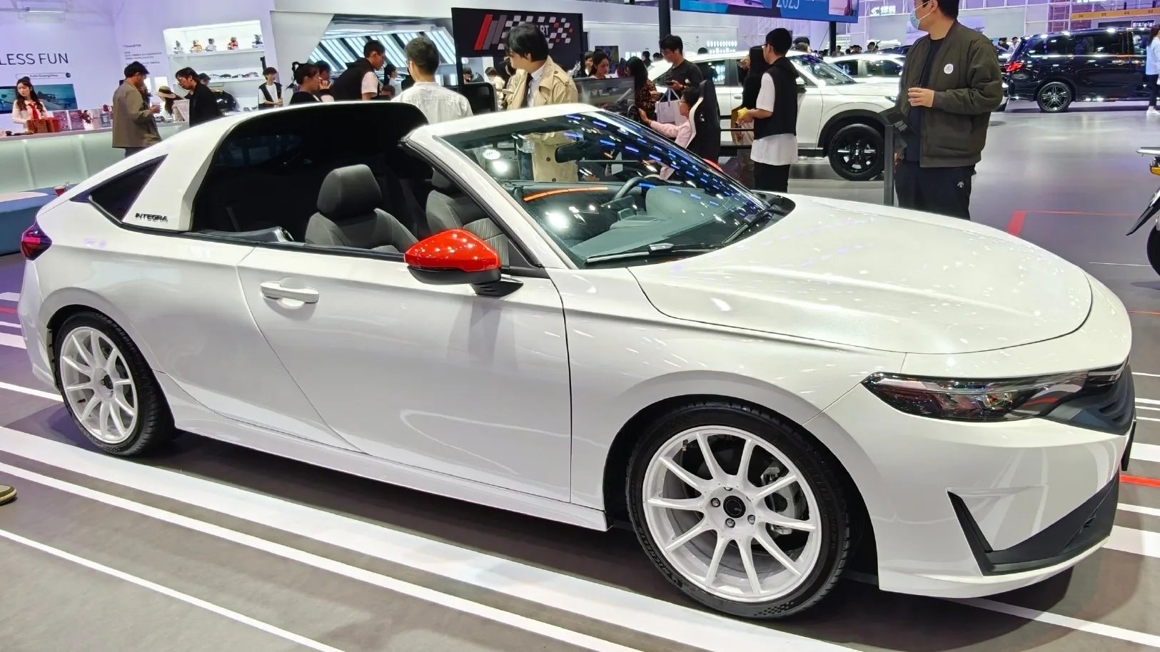 White two-door Honda Integra coupe with red side mirror and sporty white rims at an auto show.
