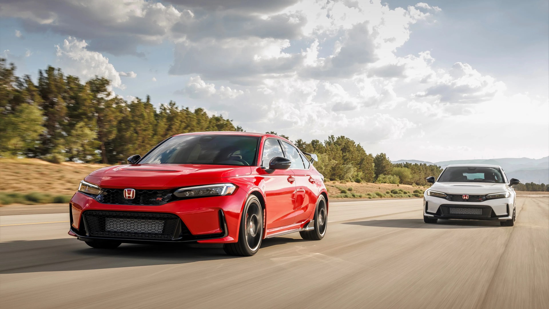Red and white Honda Civic Type R cars driving on a road with trees and cloudy sky in the background.