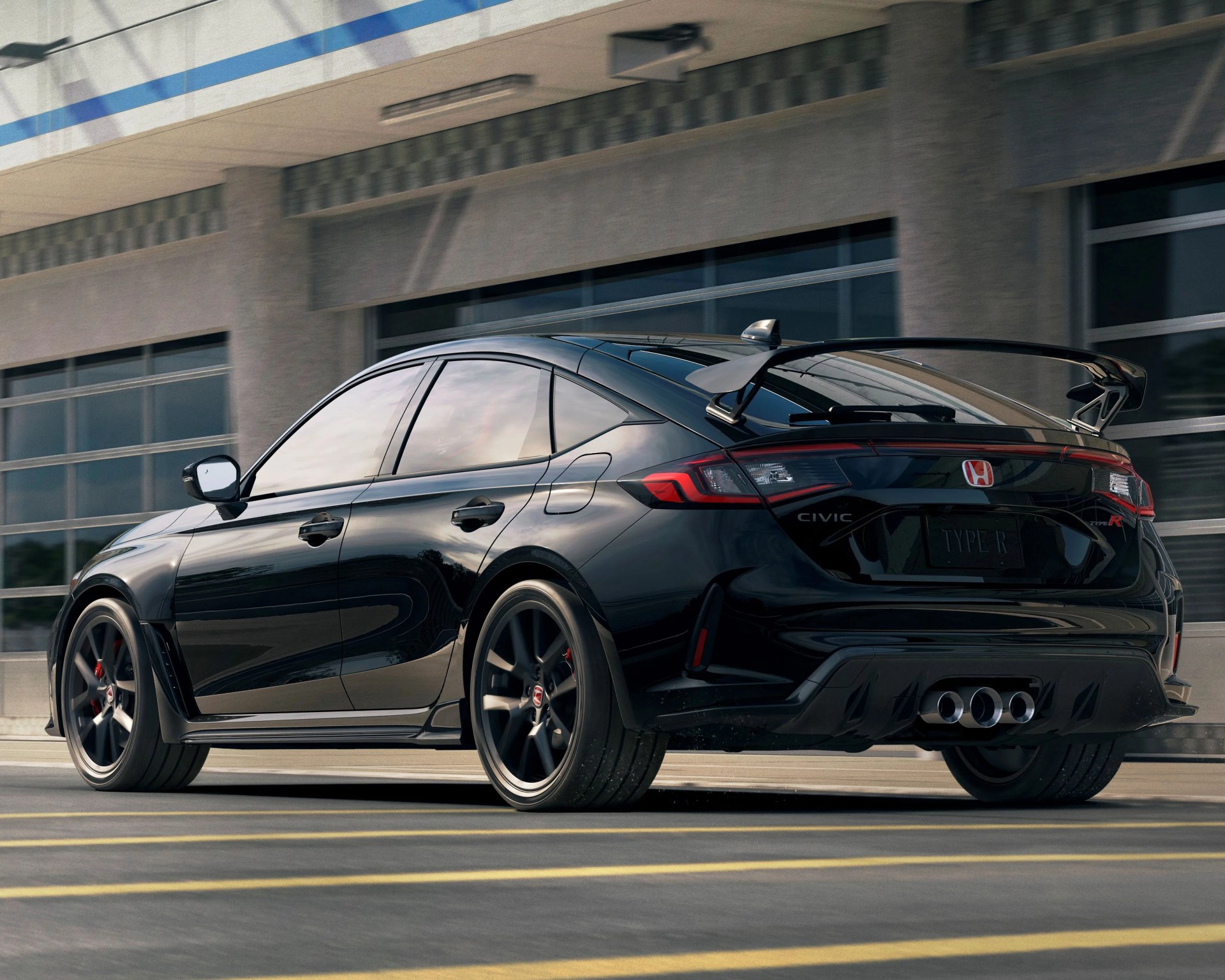 Glossy black Honda Civic Type R sedan with large rear spoiler and triple exhaust tips on a city street.
