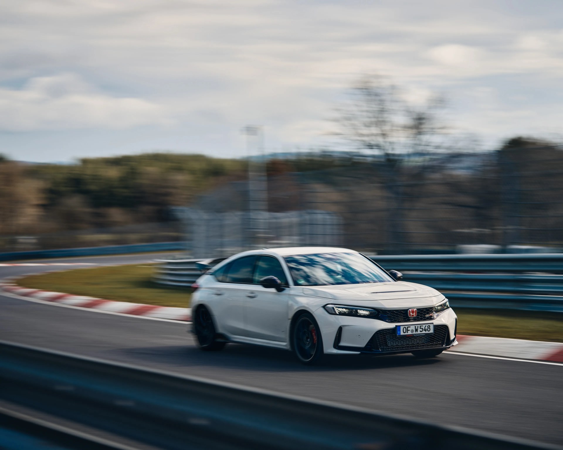 White Honda Civic Type R sedan with black wheels driving on a racetrack with blurred background.