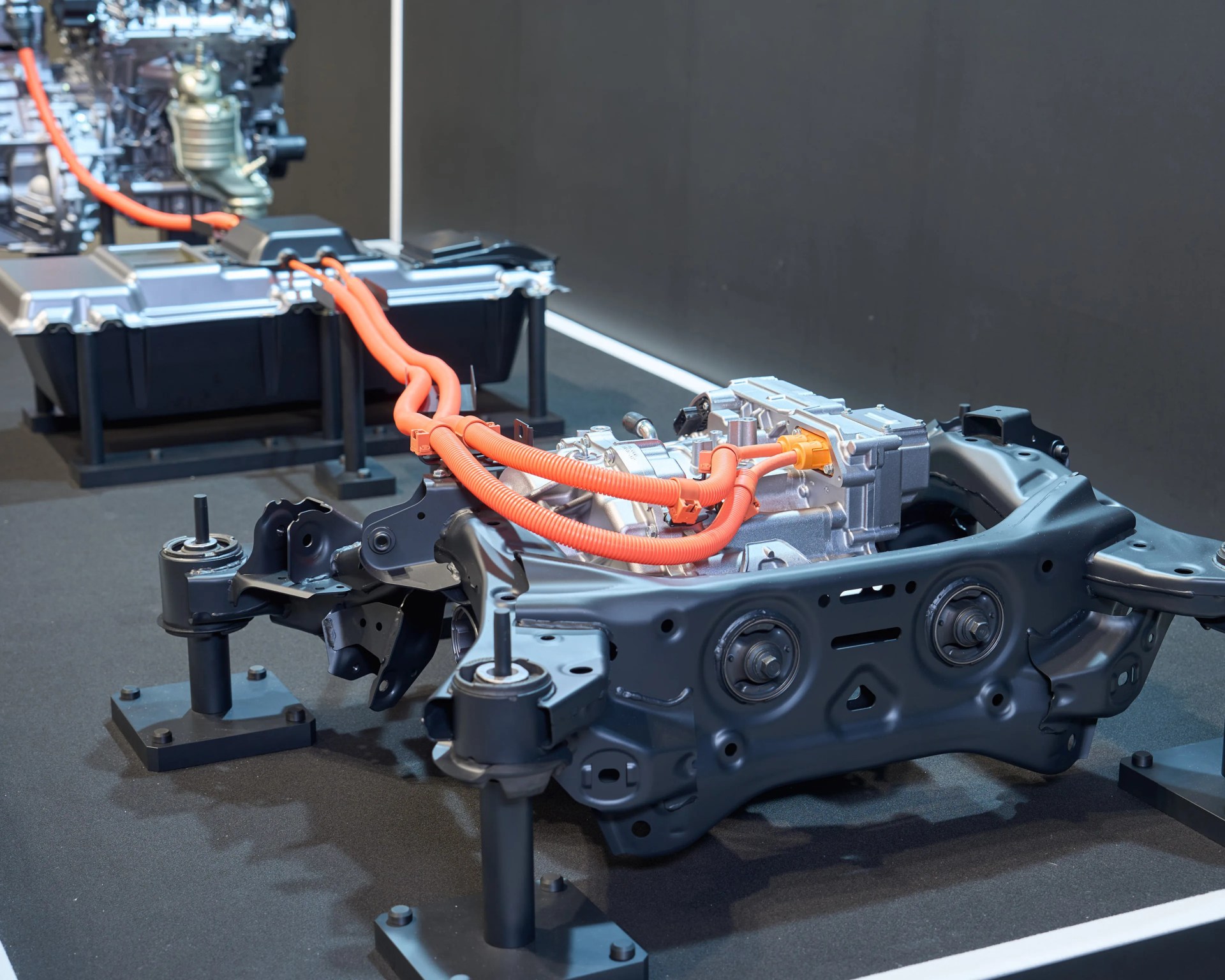 Electric vehicle battery pack and motor assembly with orange high-voltage cables on display stands.