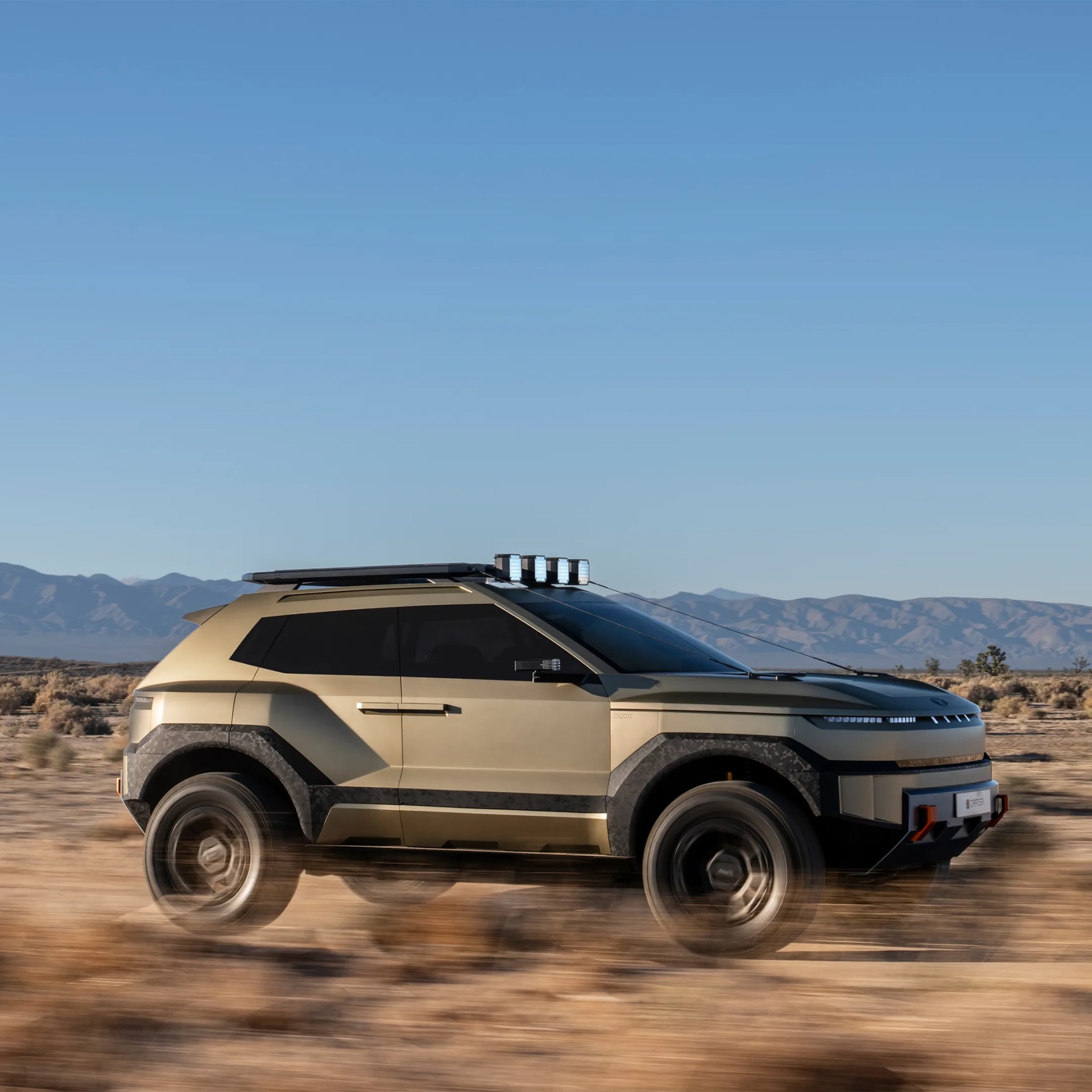 Matte olive-green off-road SUV with black trim and roof lights driving in a desert landscape.