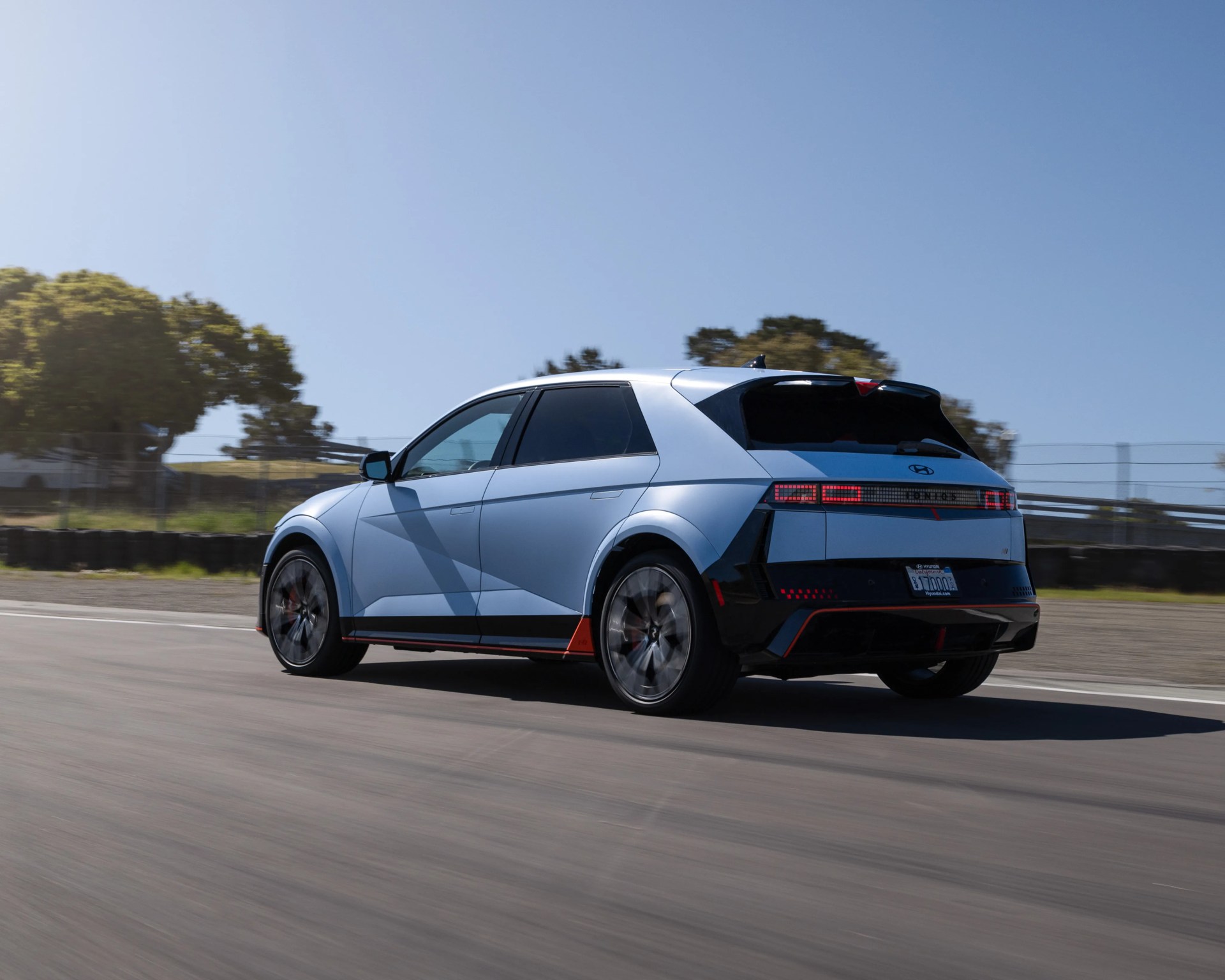 Light blue Hyundai Ioniq 5 electric SUV driving on a road with trees and clear sky in the background.