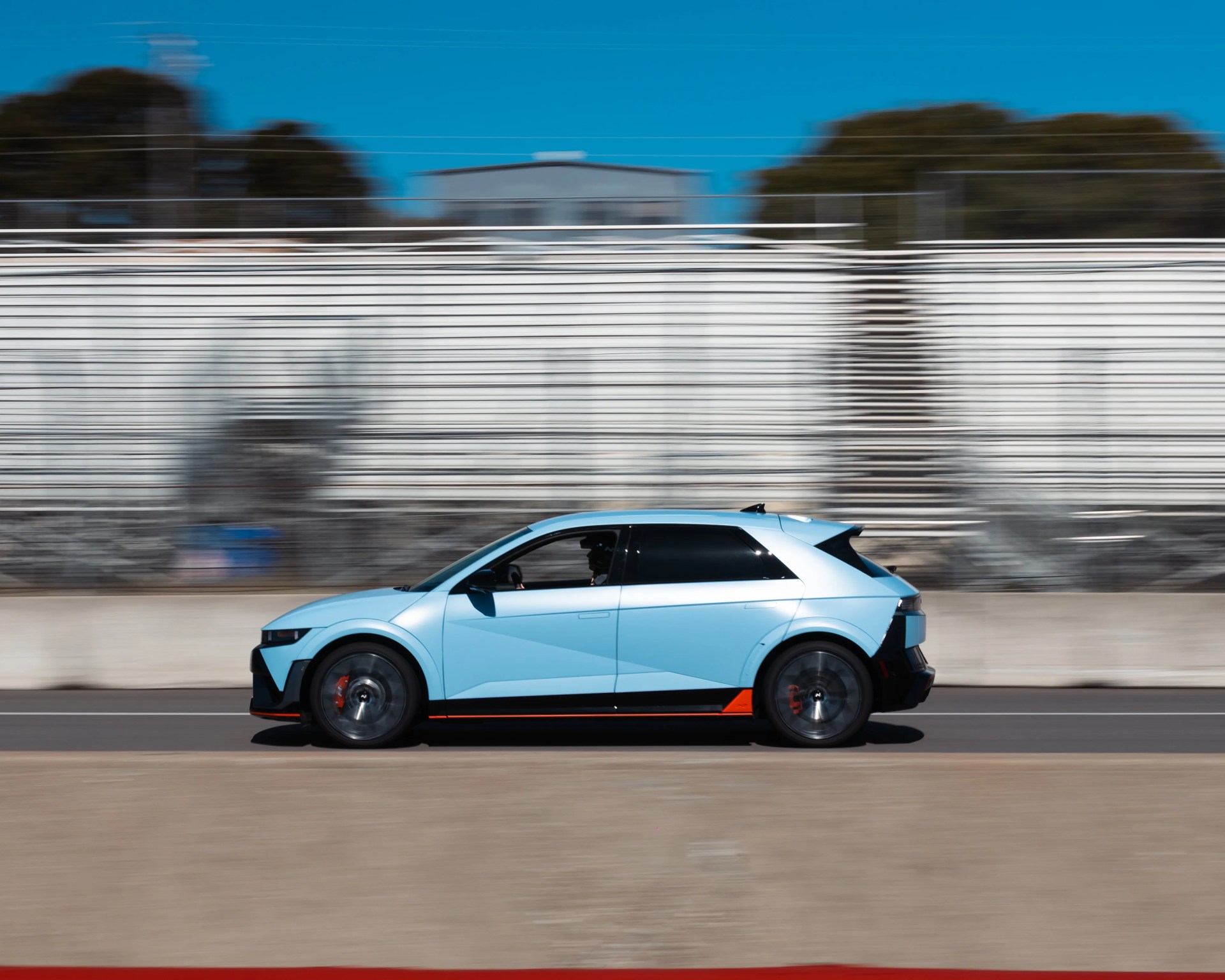 Light blue compact electric hatchback car with black and orange accents driving on a racetrack.
