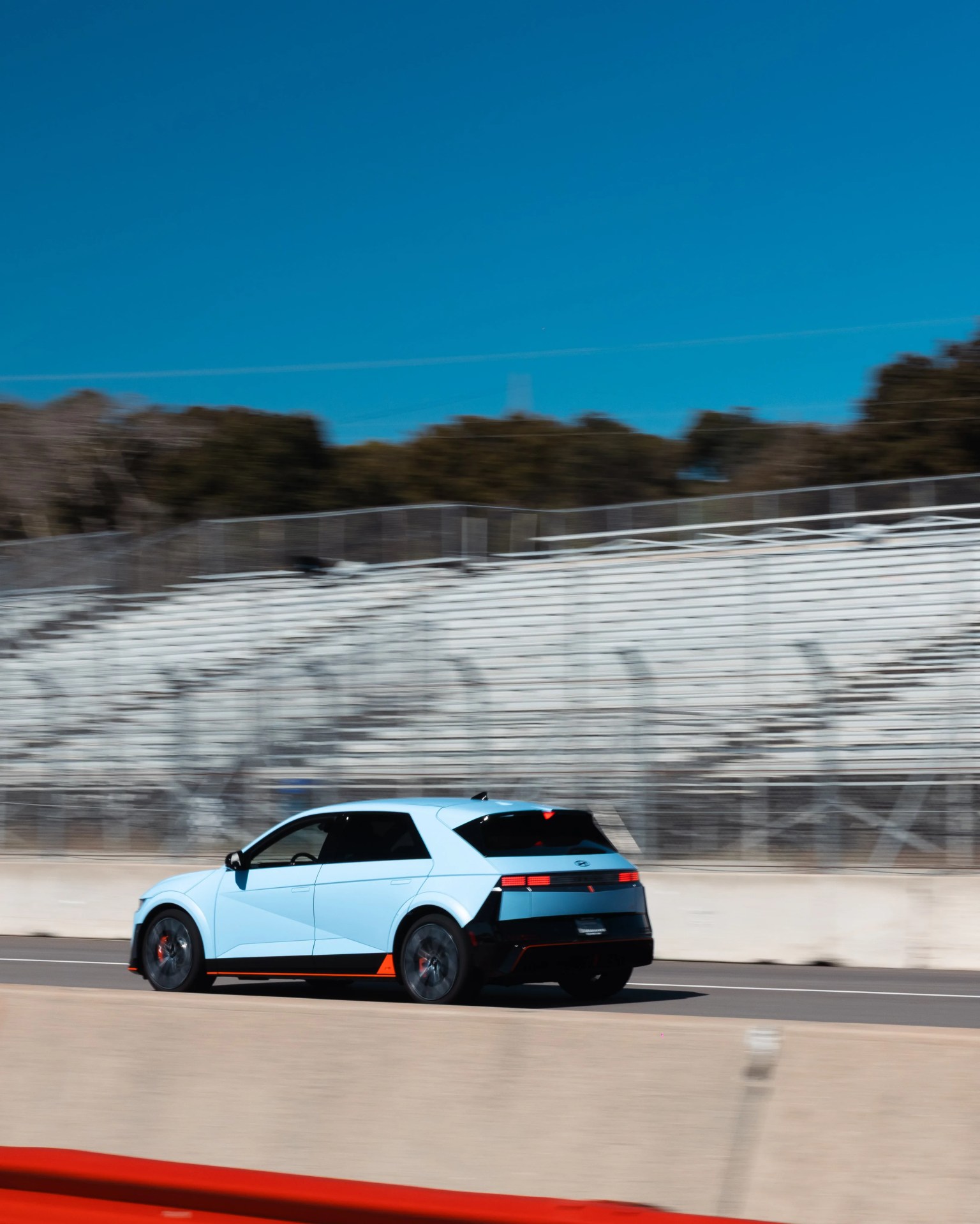 Light blue Hyundai Ioniq 5 electric car driving on a racetrack with blurred background.