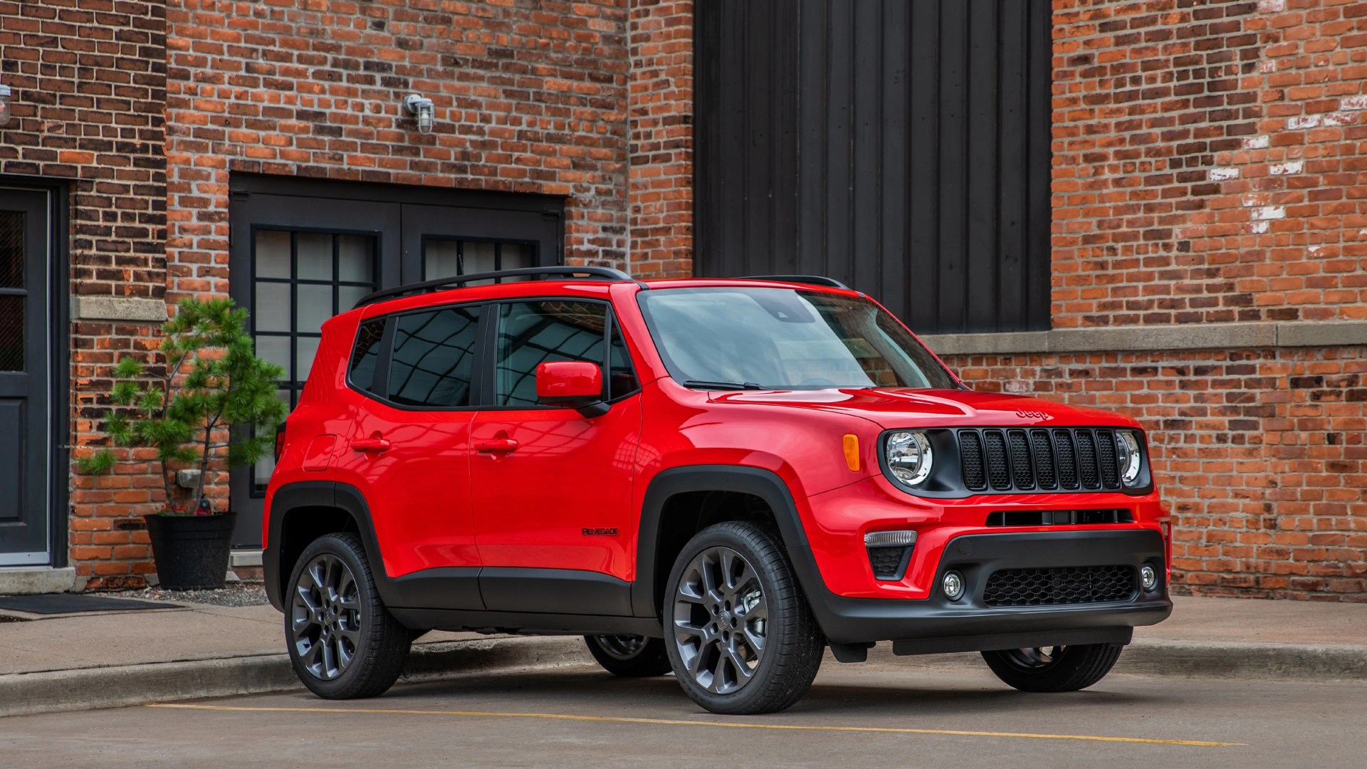 Red Jeep Renegade SUV parked on a street in front of a brick building.