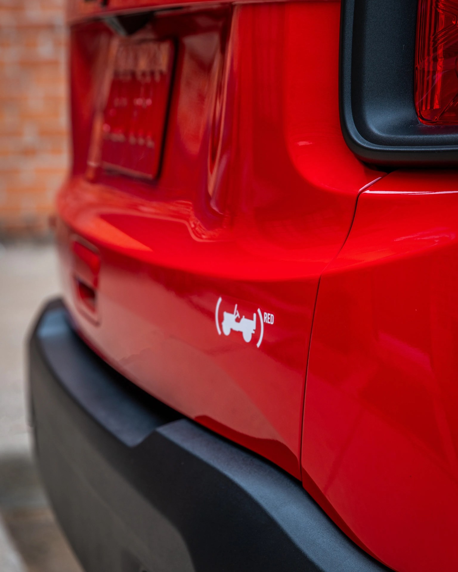 Close-up of a red vehicle's rear bumper with a white (RED) logo decal above the black plastic trim.