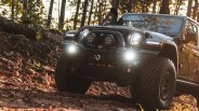 Black off-road Jeep with large tires and bright front lights driving on a rocky forest trail.