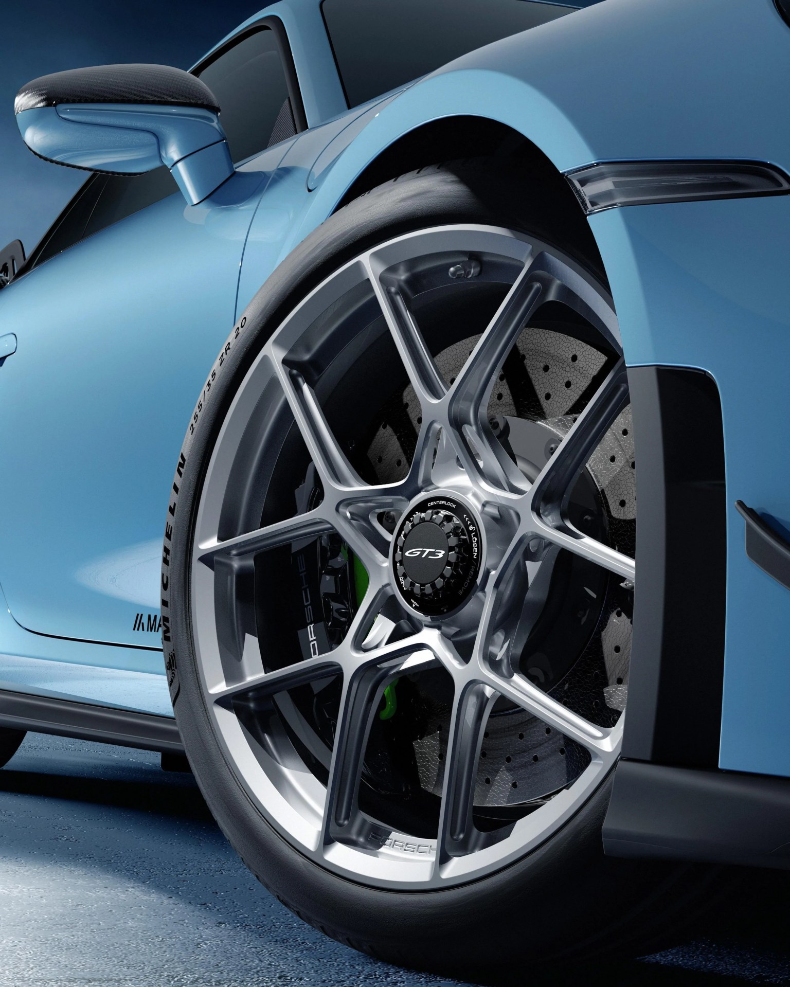 Close-up of a silver multi-spoke GT3 alloy wheel with Michelin tire on a light blue sports car.