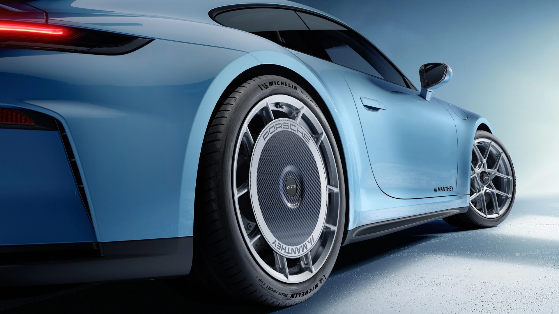 Light blue Porsche GT3 with custom Manthey carbon fiber wheel cover on rear tire.