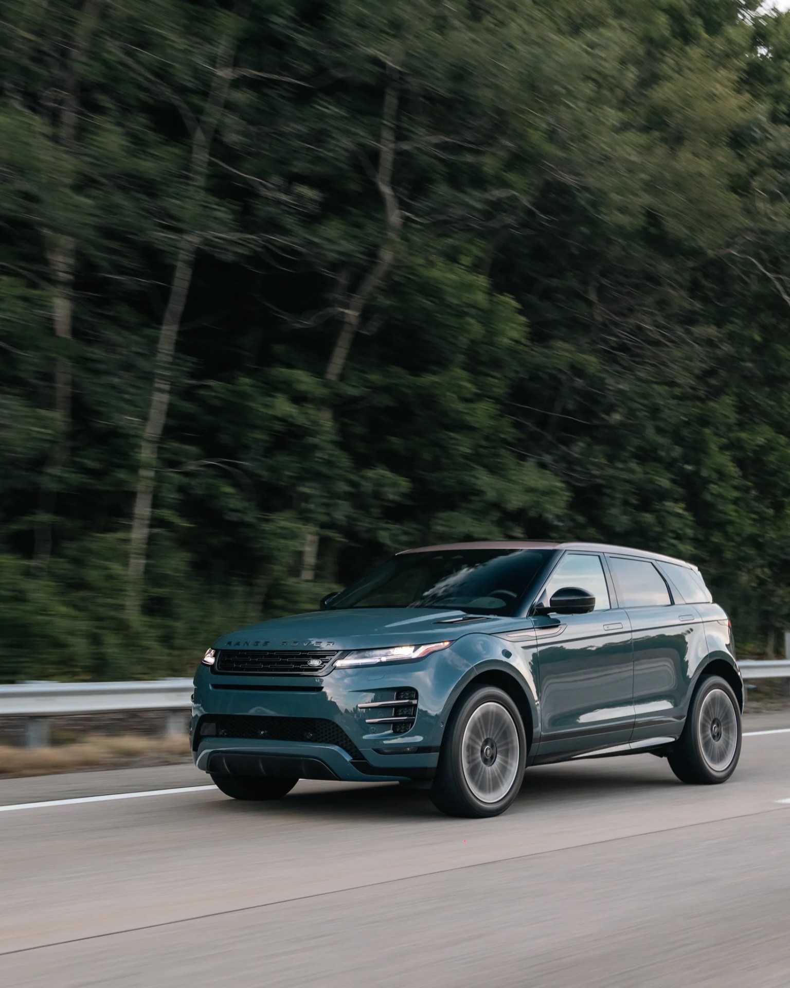 Blue Range Rover SUV driving on a highway with blurred trees in the background.