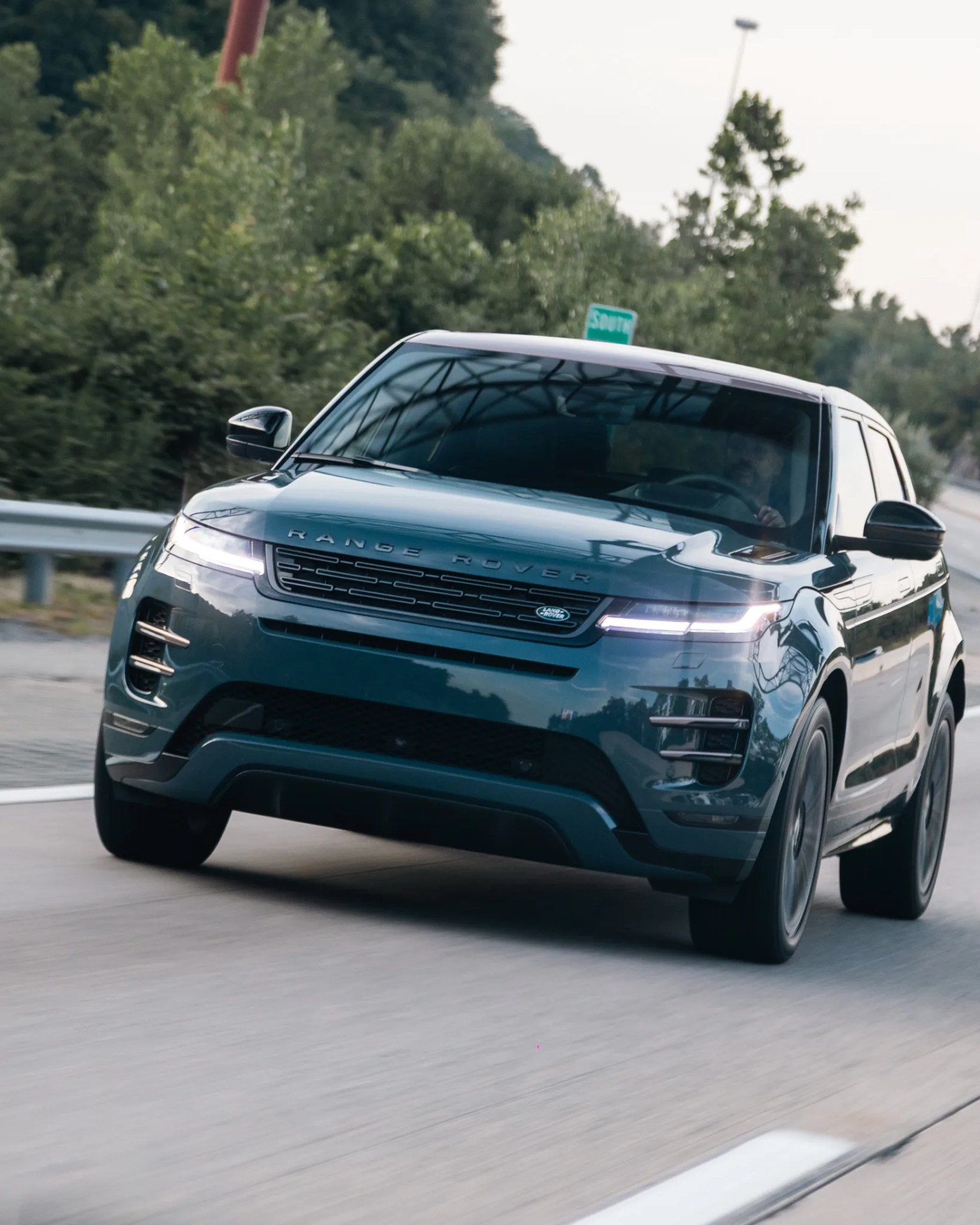 Dark green Range Rover SUV driving on a highway with trees in the background.