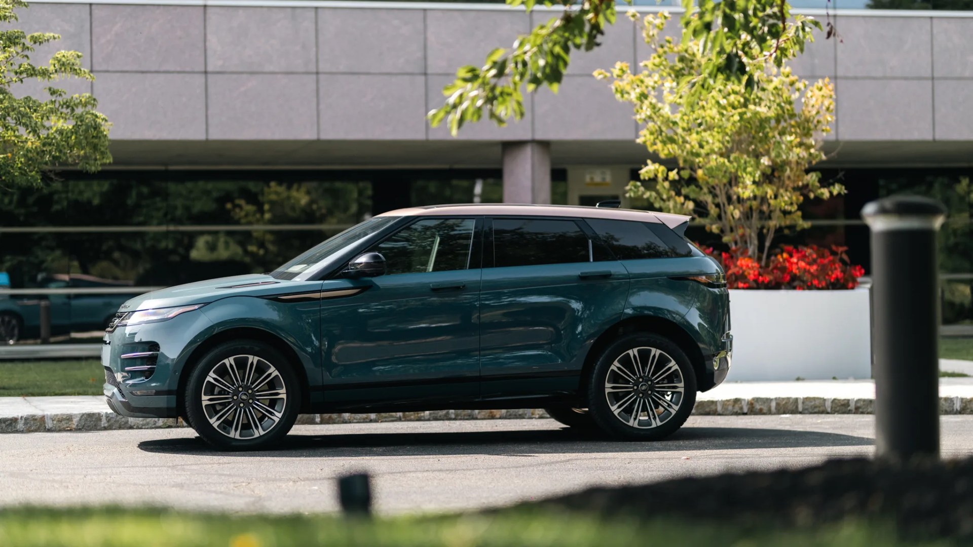 Teal and beige Range Rover Evoque SUV parked on a street with a building and greenery in the background.