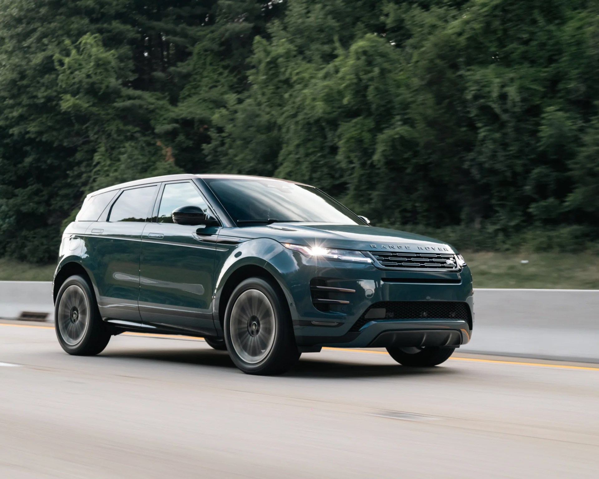 Dark green Range Rover SUV driving on a highway with trees in the background.