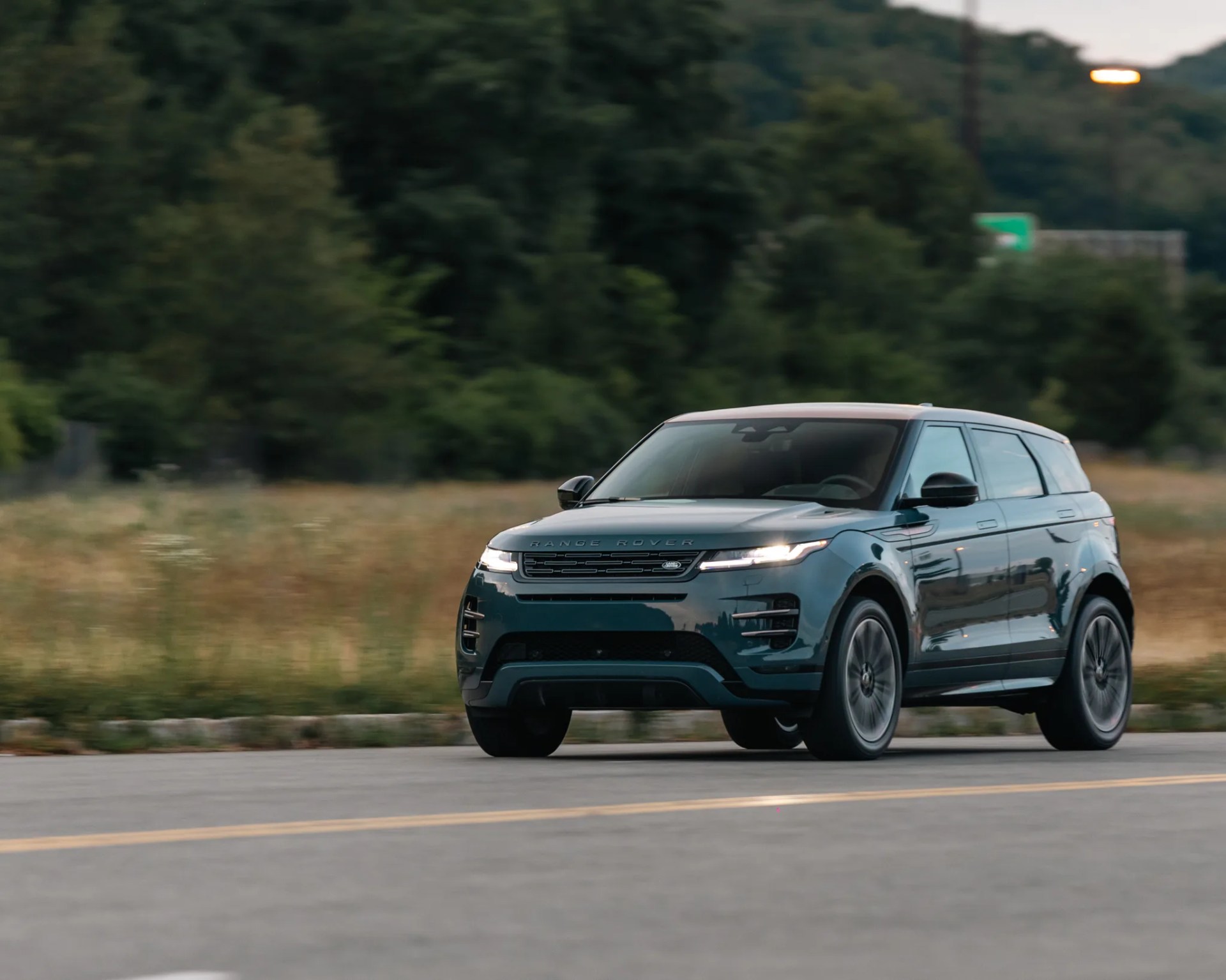 Dark green Range Rover SUV driving on a road with trees and grass in the background.