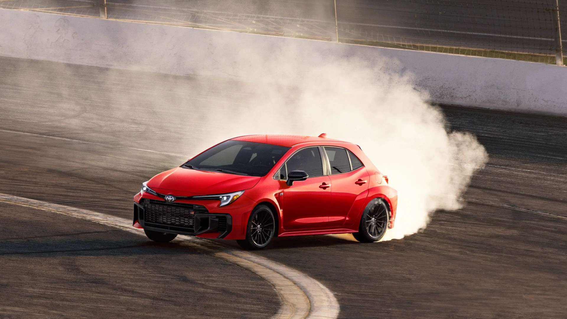 Red Toyota GR hatchback drifting on a race track with smoke coming from the rear tires.