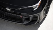 Close-up of the front grille and headlight of a black Toyota GR car with black alloy wheel on a concrete surface.