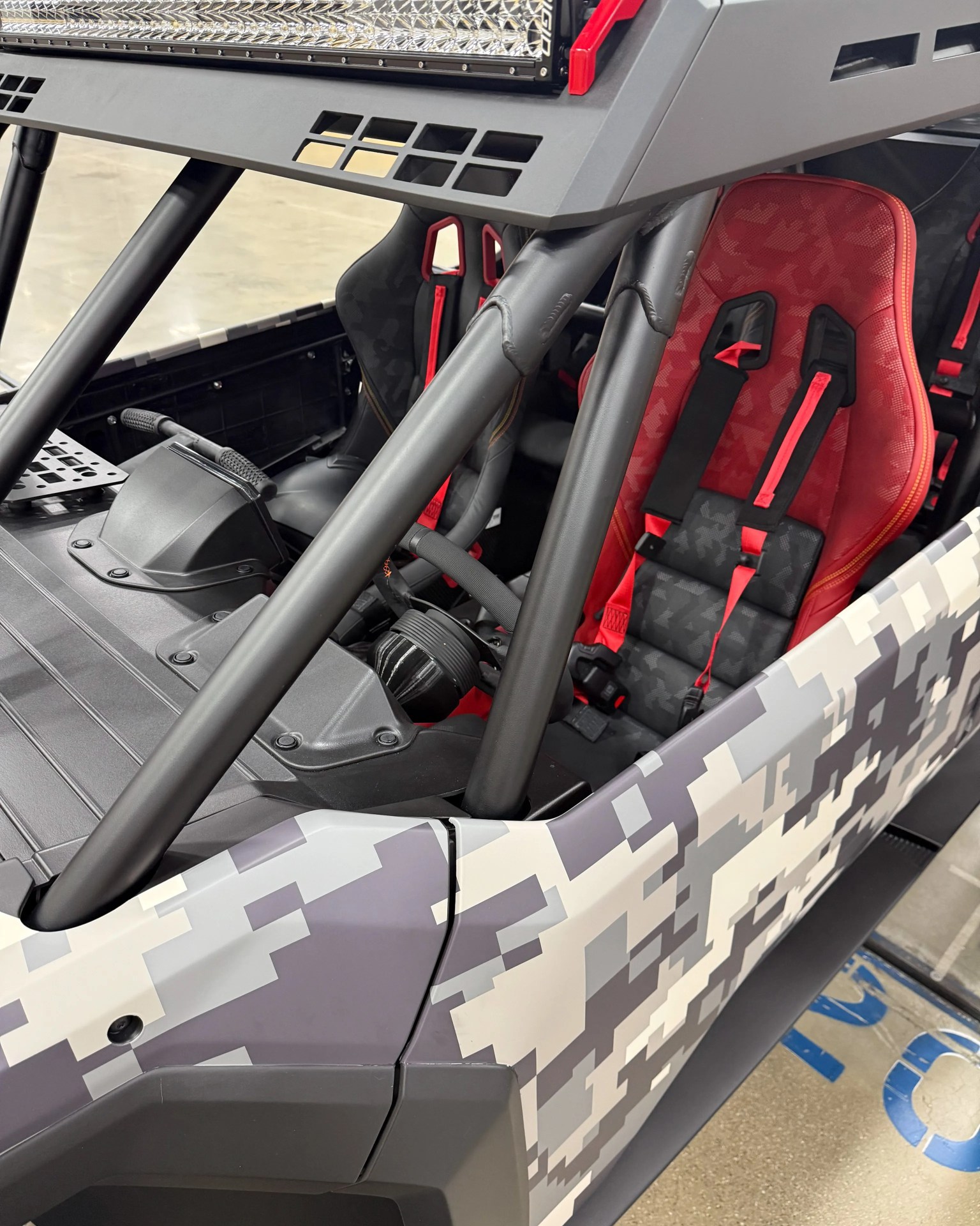 Off-road vehicle interior with red and black racing seats and digital camouflage exterior panels.