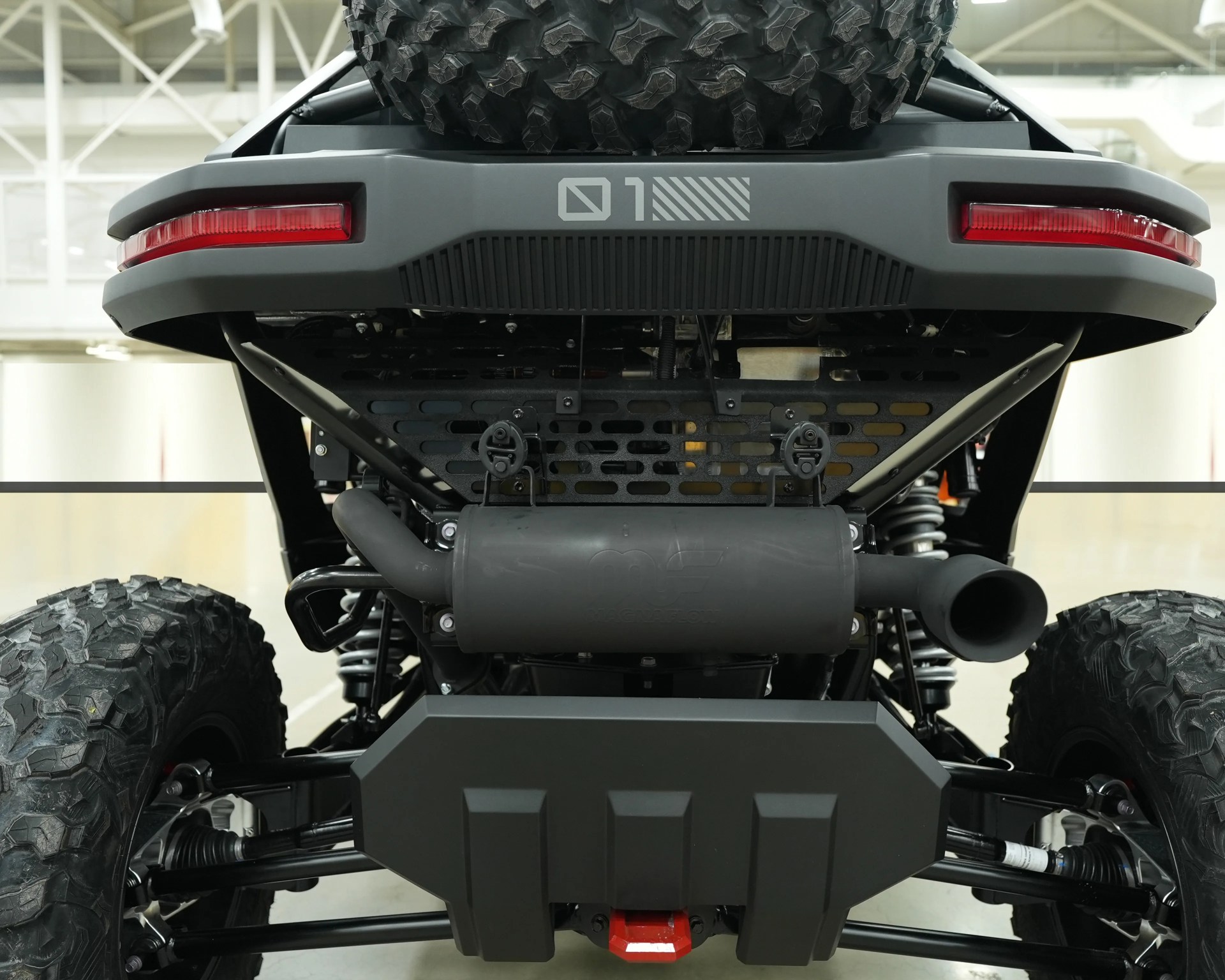 Rear view of an off-road vehicle showing large knobby tires, exhaust system, and suspension components.