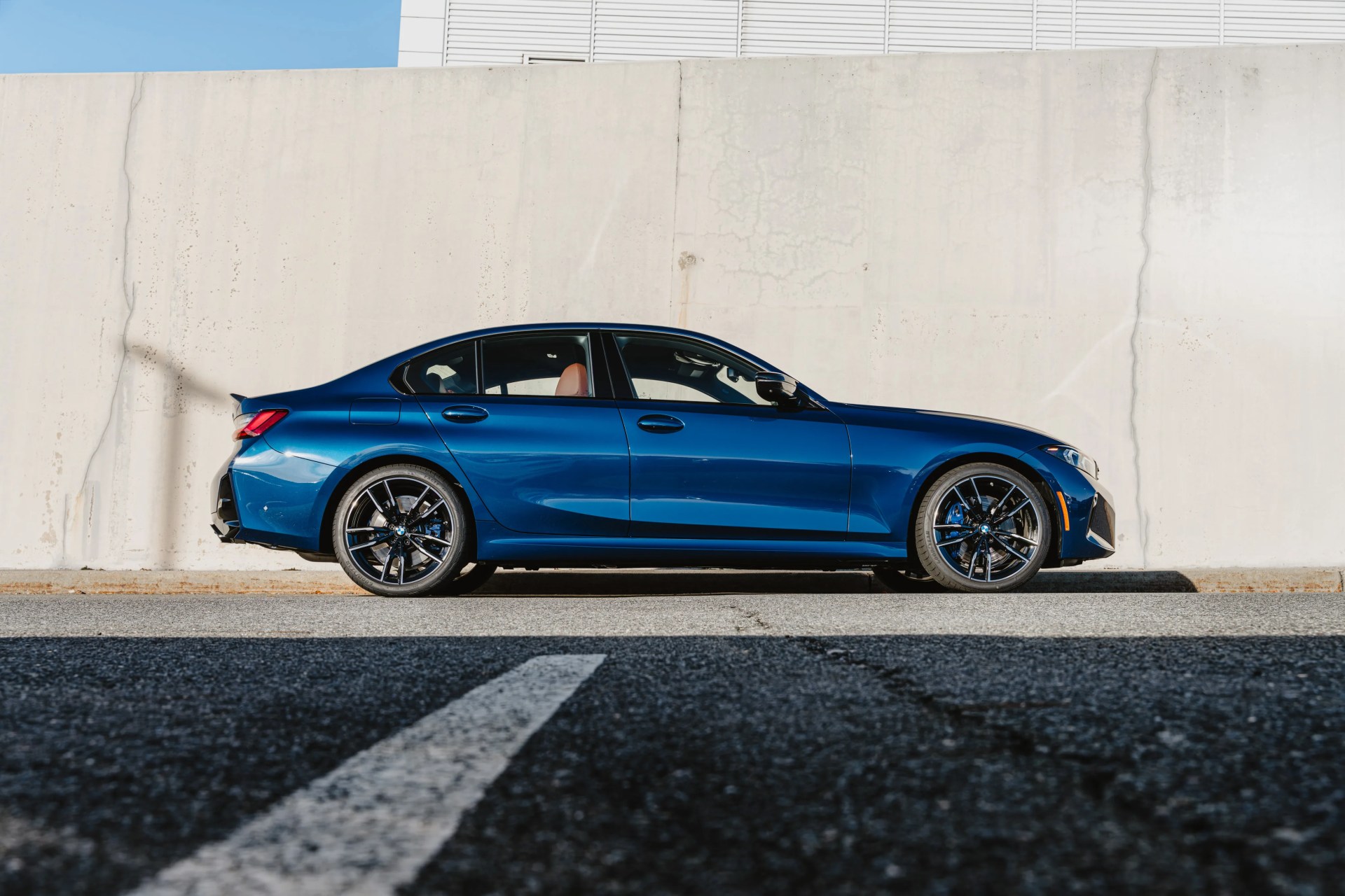 Blue sedan with black alloy wheels parked in front of a concrete wall.