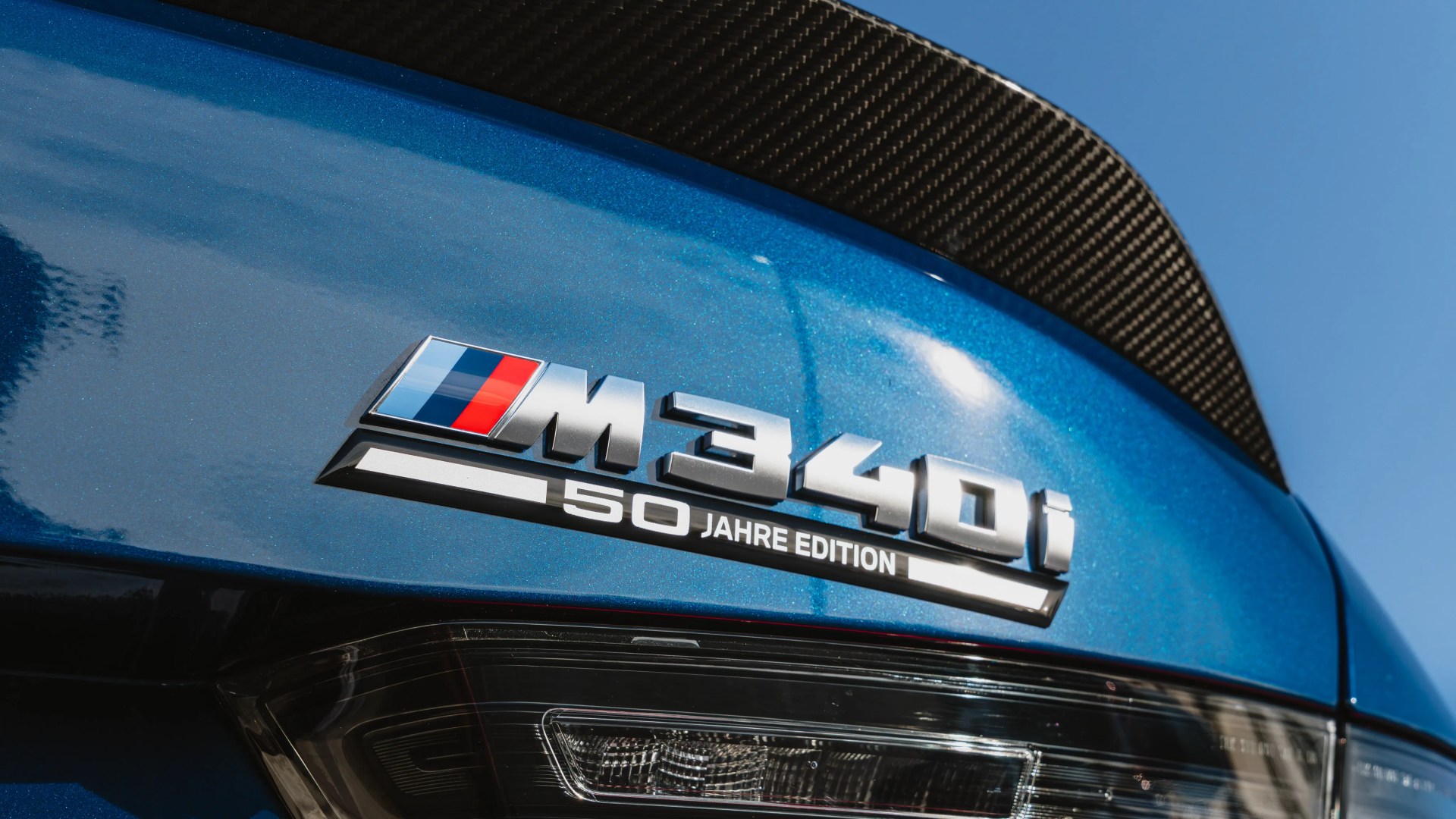 Close-up of a blue BMW M340i 50 Jahre Edition badge with a carbon fiber spoiler above.