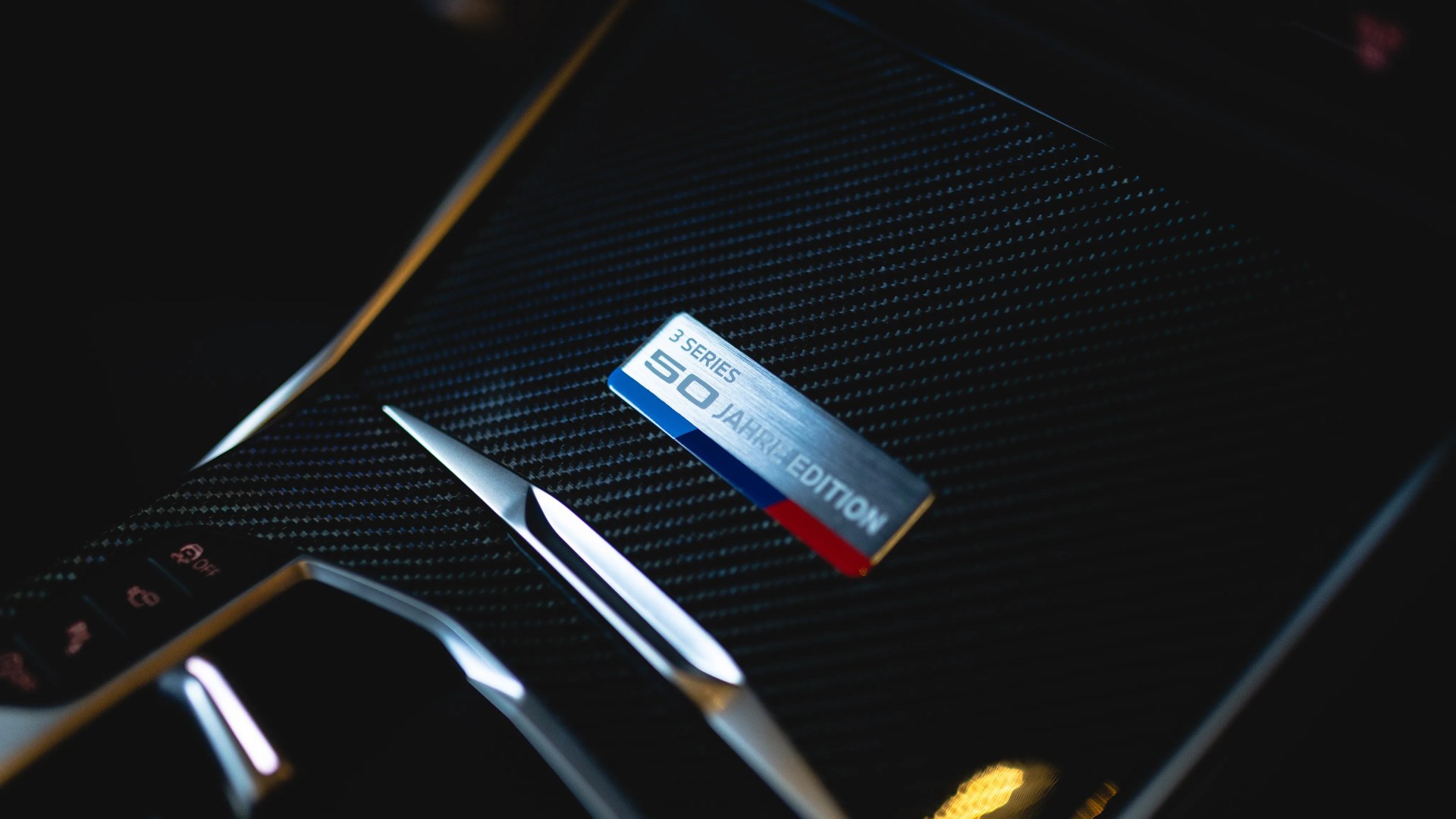 Close-up of a carbon fiber car interior panel with a "3 Series 50 Jahre Edition" badge and metallic trim.