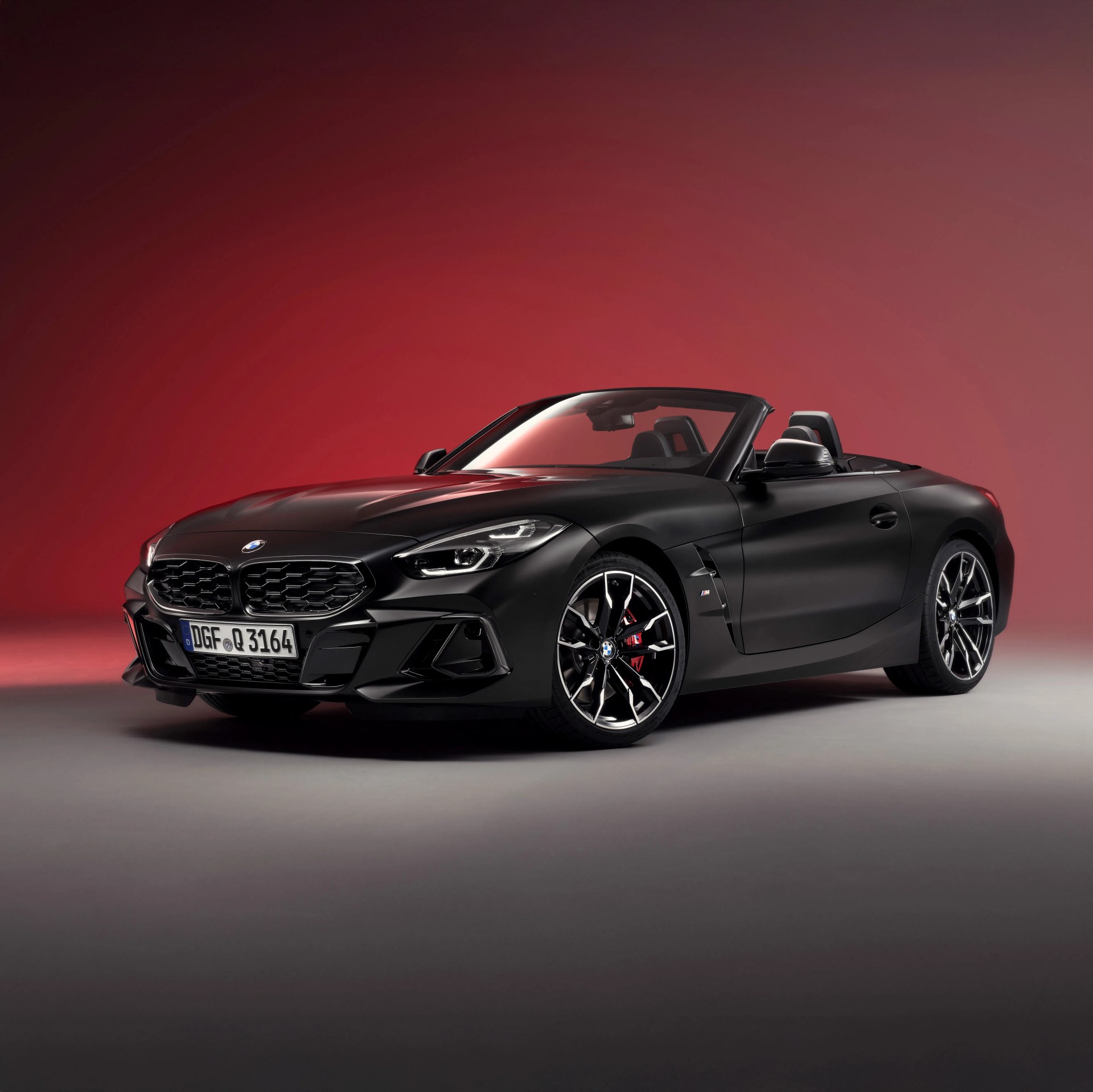Matte black BMW convertible sports car with red brake calipers on gray floor and red background.