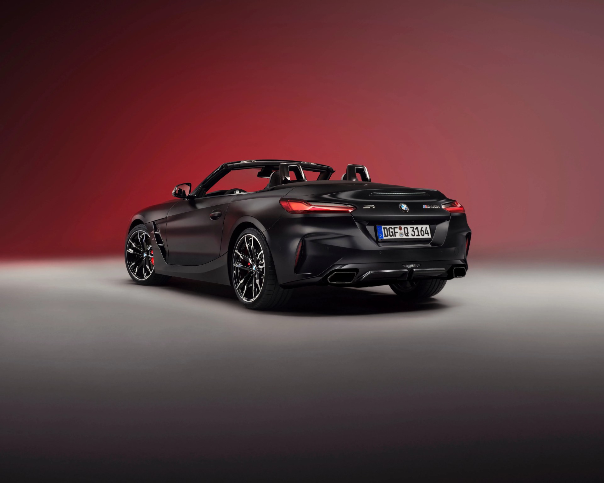 Matte black BMW Z4 M40i convertible with black and silver wheels on a gradient red and gray background.