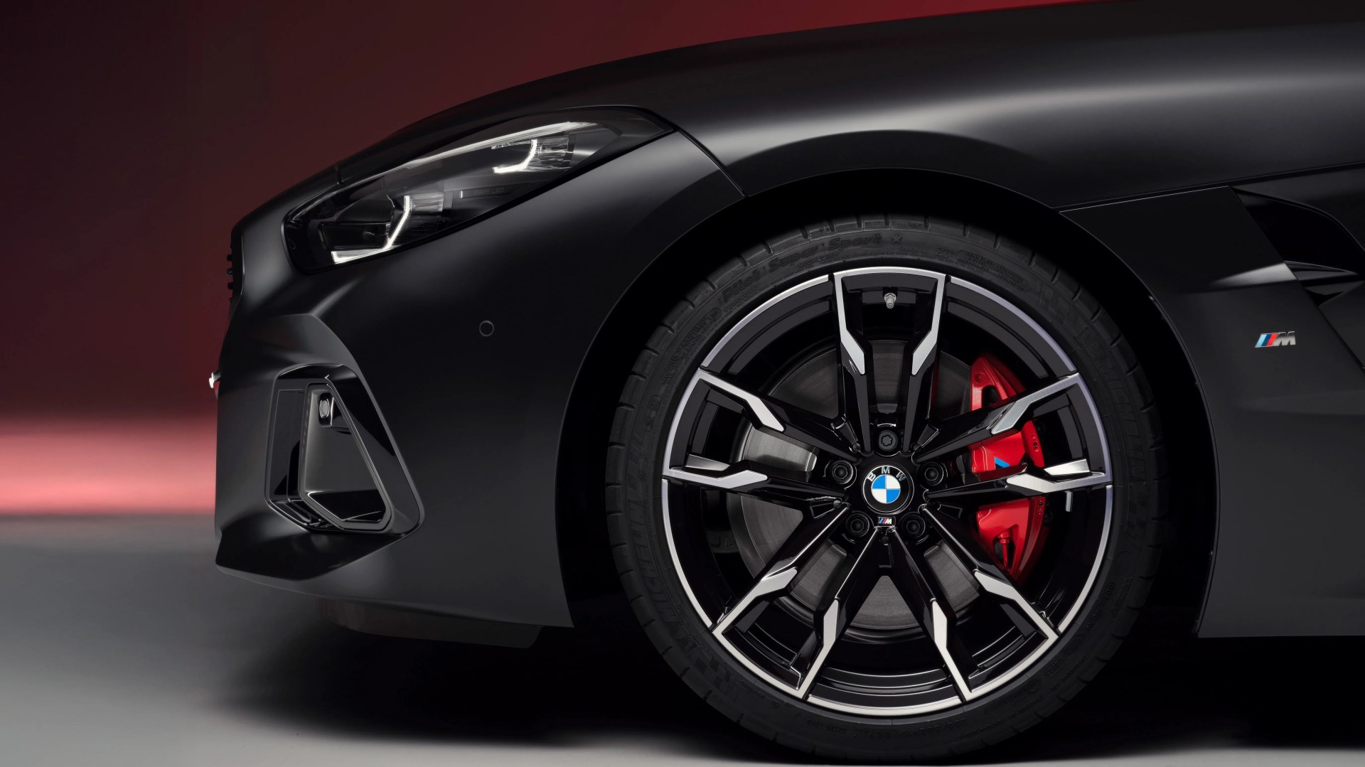 Close-up of a black BMW car front wheel with a red brake caliper and M badge on the fender.