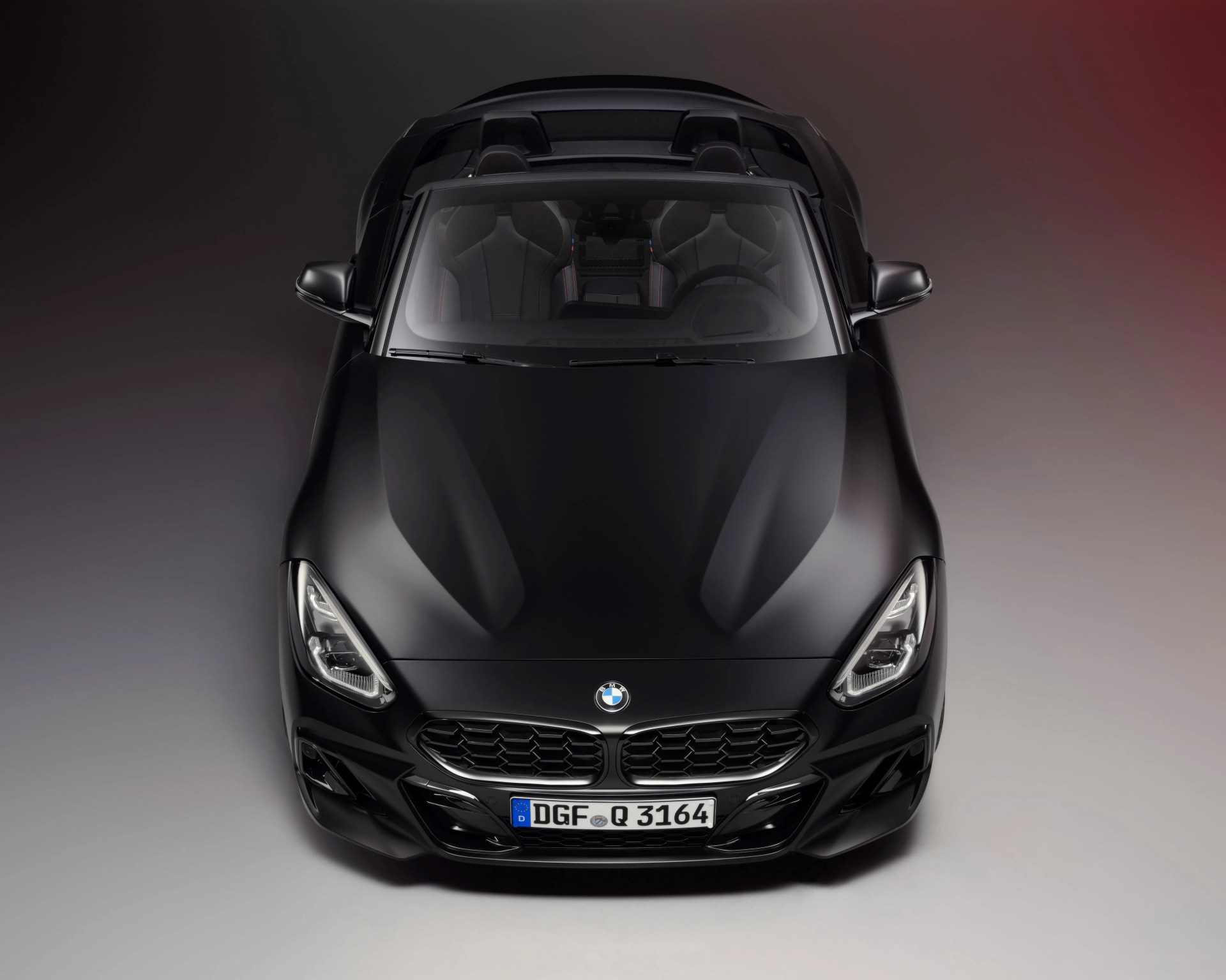Matte black BMW convertible sports car viewed from the front with visible interior seats and steering wheel.