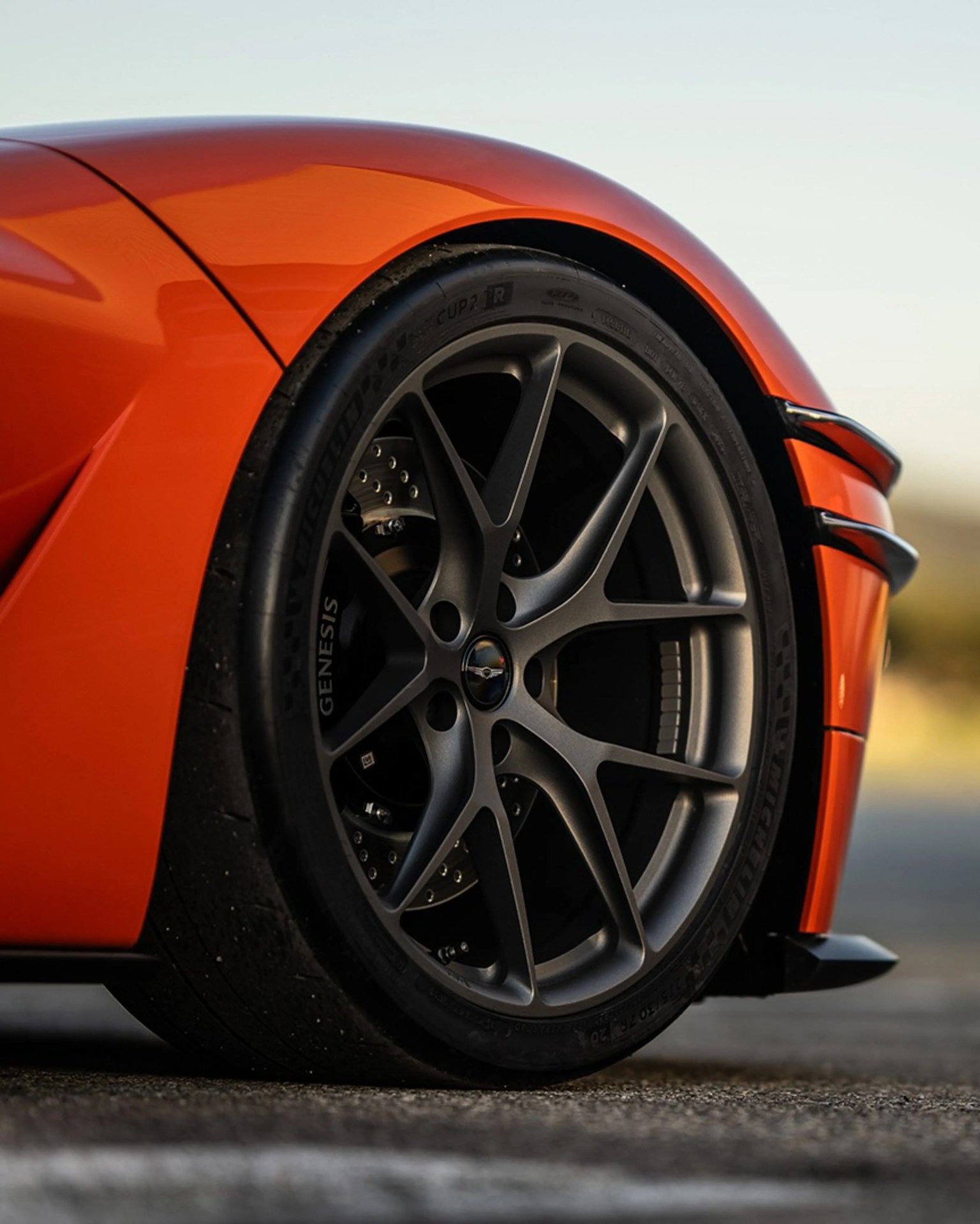 Close-up of a matte gray multi-spoke wheel with Michelin tire on an orange sports car.
