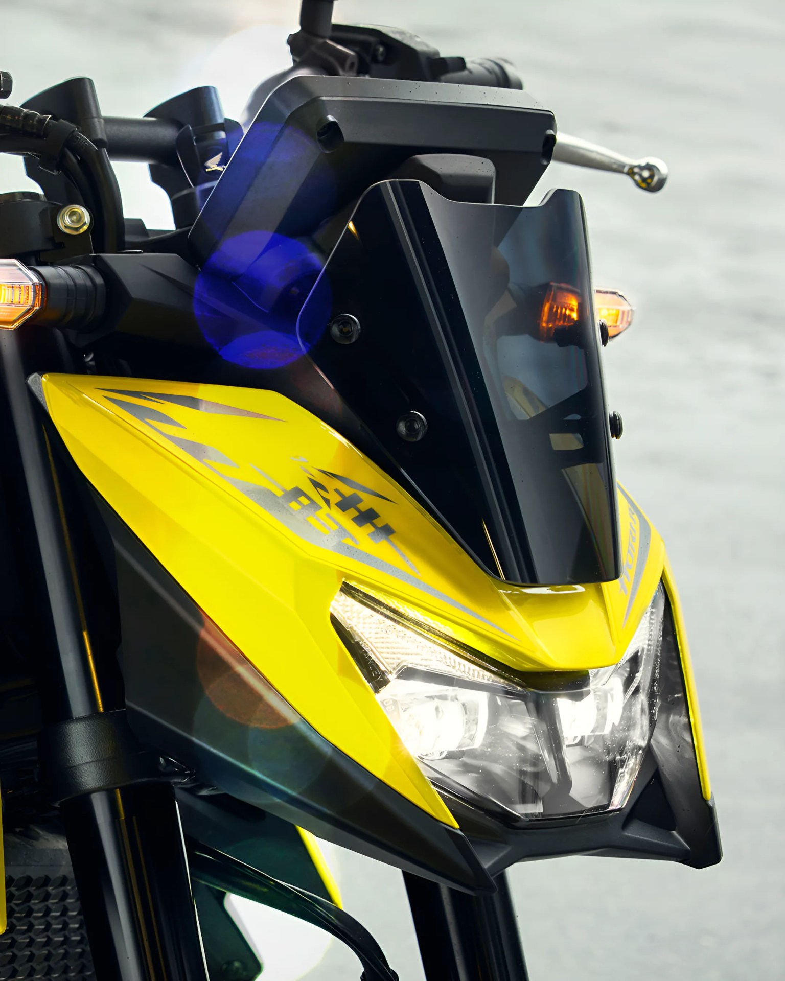 Close-up of a yellow motorcycle front with a black tinted windshield and illuminated headlights.