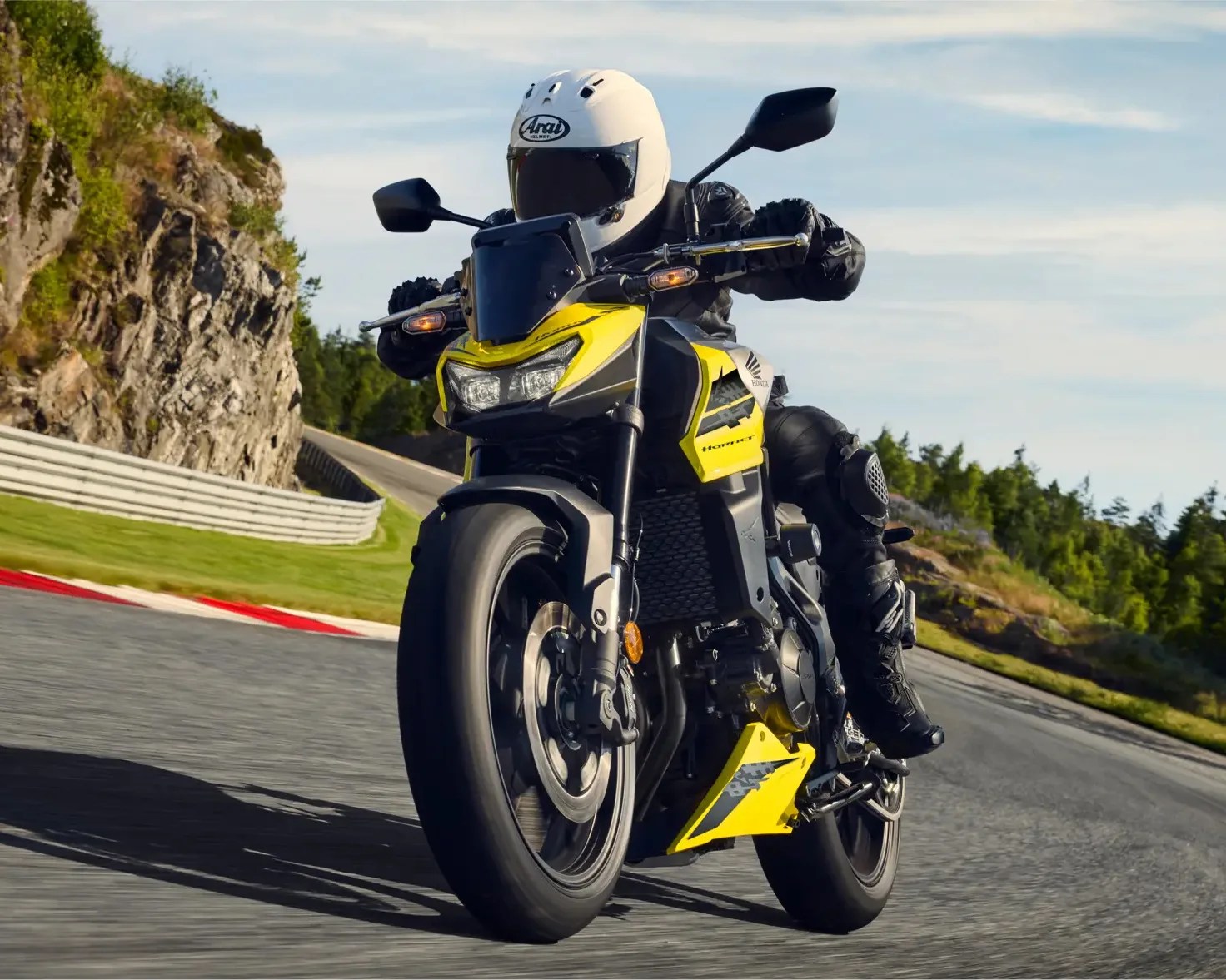 Yellow and black Honda Hornet motorcycle ridden on a curved road with rocky and forested surroundings.