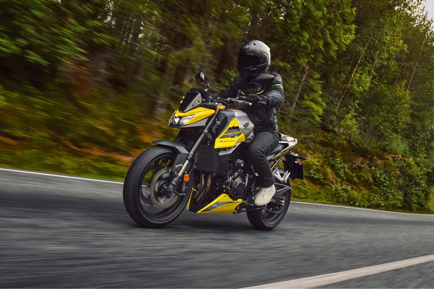Yellow and black Honda motorcycle ridden on a curved road with green trees in the background.