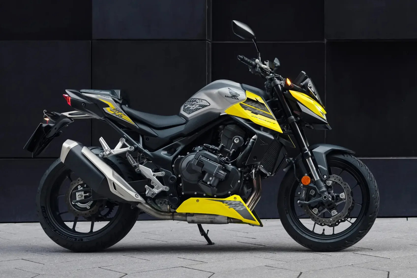 Gray and yellow Honda motorcycle with black wheels parked on a tiled surface against a dark wall.