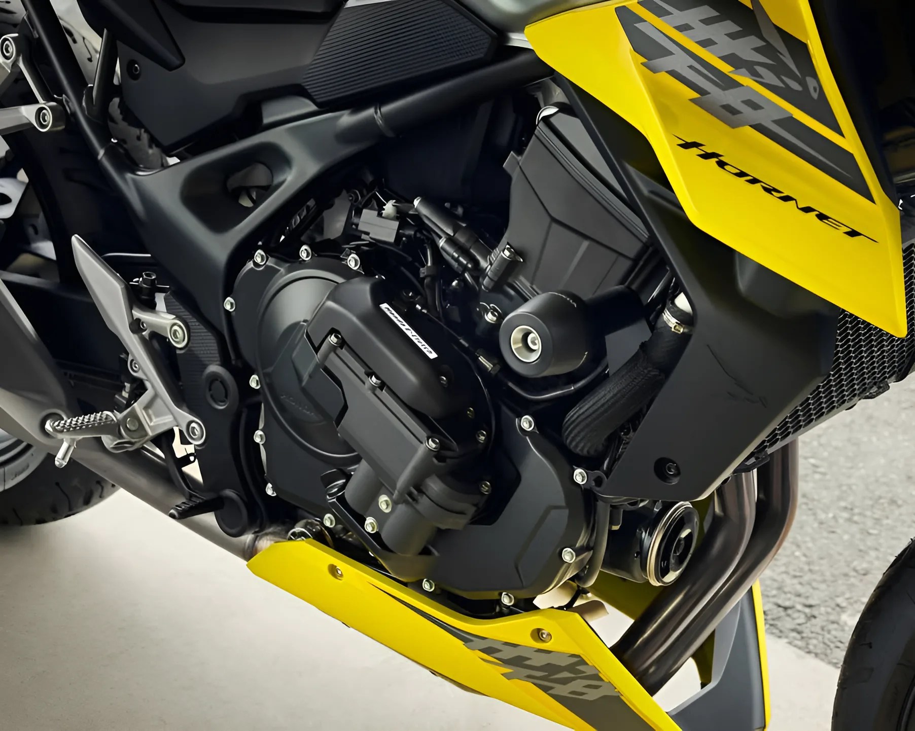 Close-up of a yellow Honda Hornet motorcycle engine and frame with visible exhaust pipes and footpeg.