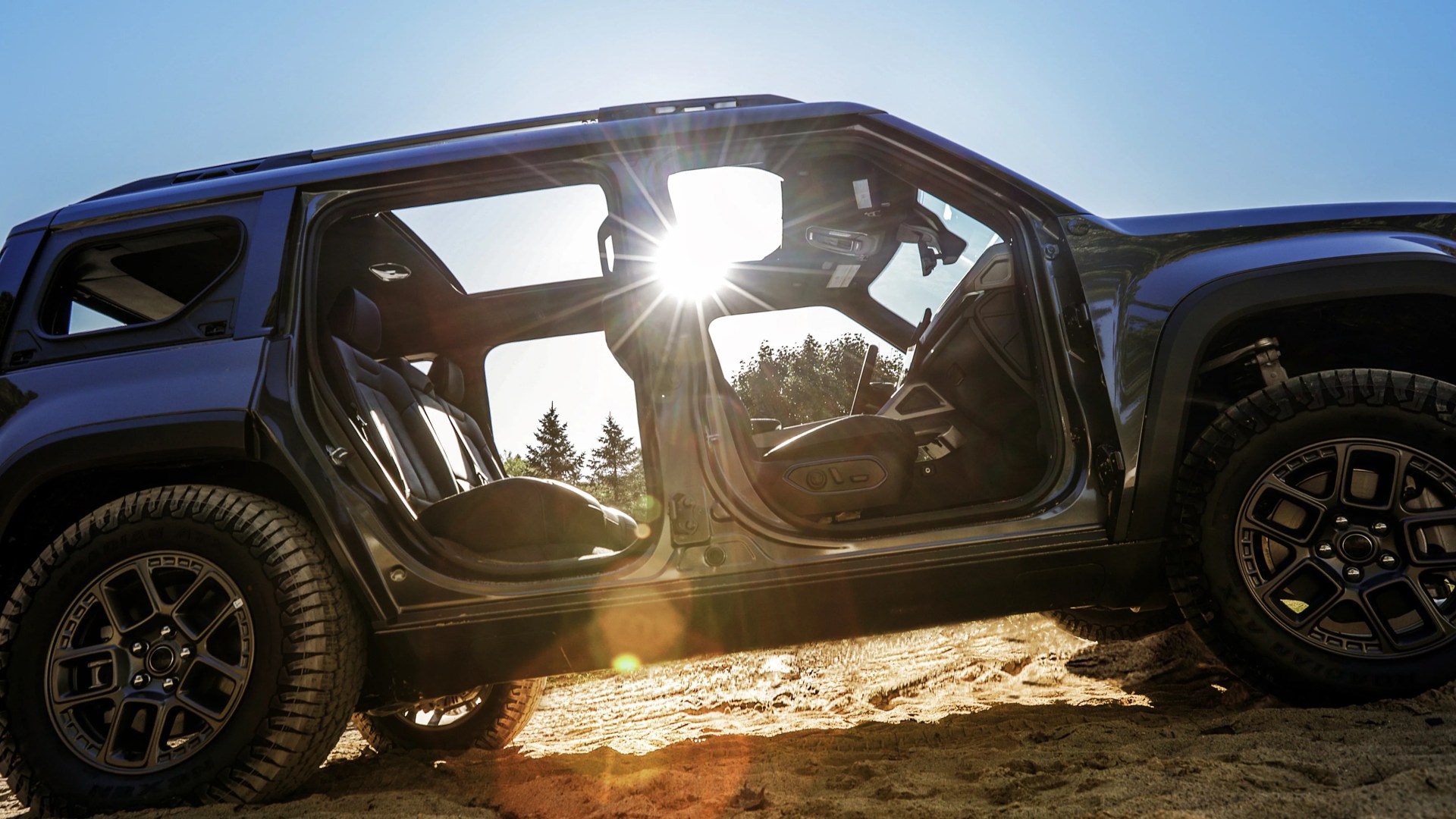 Black off-road SUV with open doors and visible interior seats on sandy terrain with sun glare.