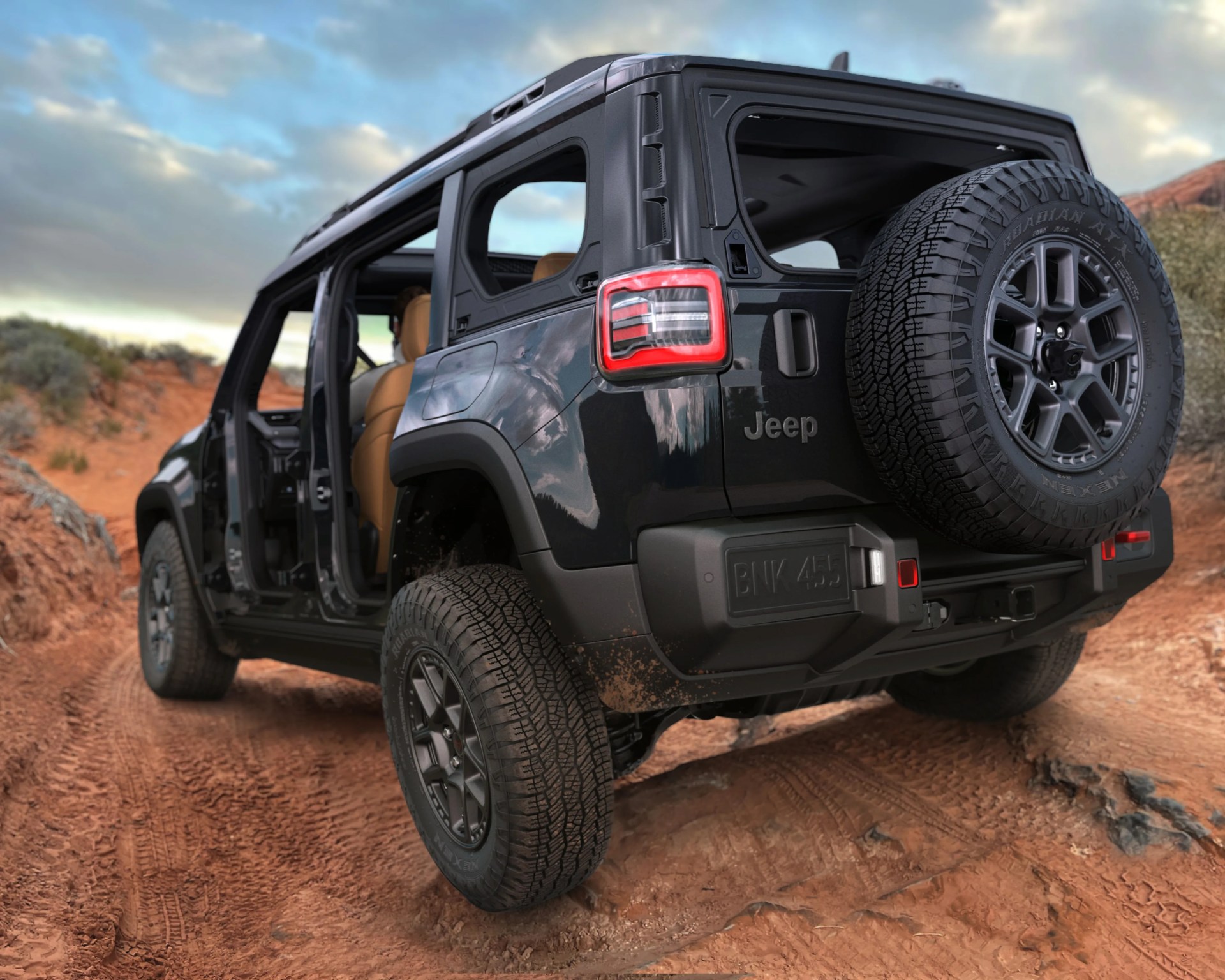 Black Jeep SUV with tan interior and no doors on a dirt trail in a desert landscape.