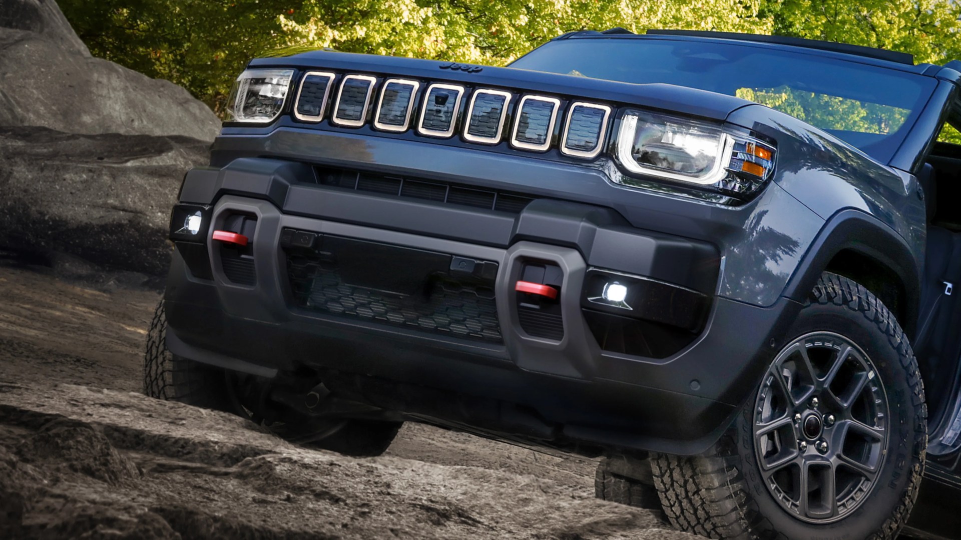 Front view of a dark gray Jeep SUV with LED headlights and off-road tires on rocky terrain.