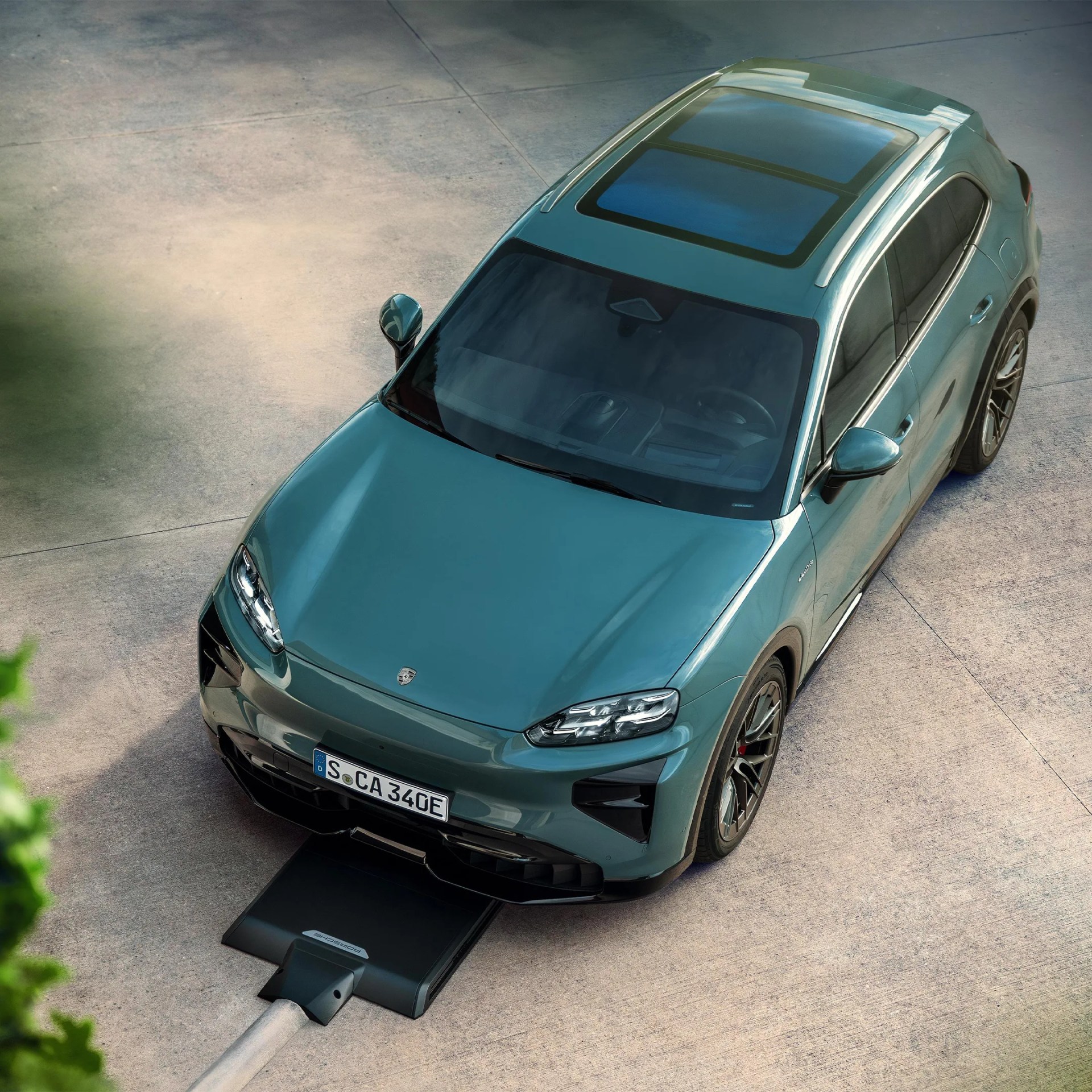 Teal Porsche electric SUV with panoramic sunroof charging on a concrete surface.