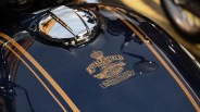 Glossy dark blue motorcycle fuel tank with gold Royal Enfield logo and twin gold stripes.