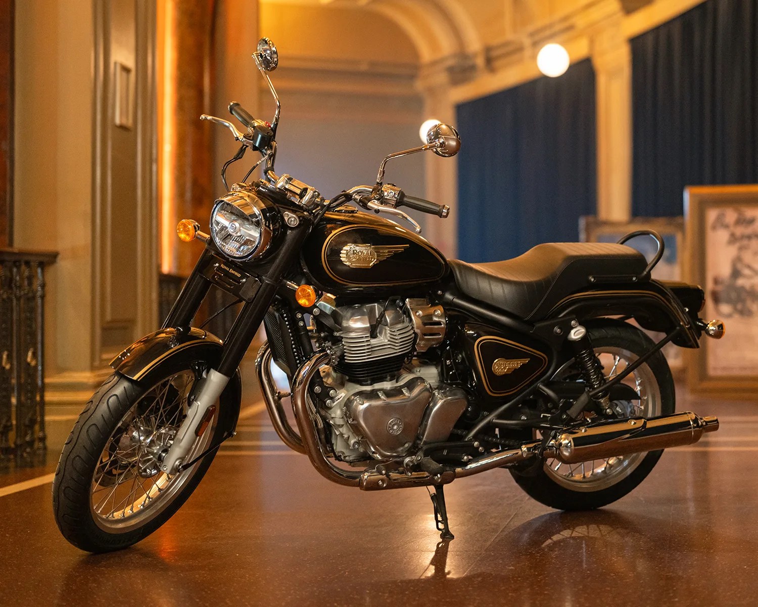 Black and chrome Royal Enfield motorcycle with gold accents parked indoors on a polished floor.