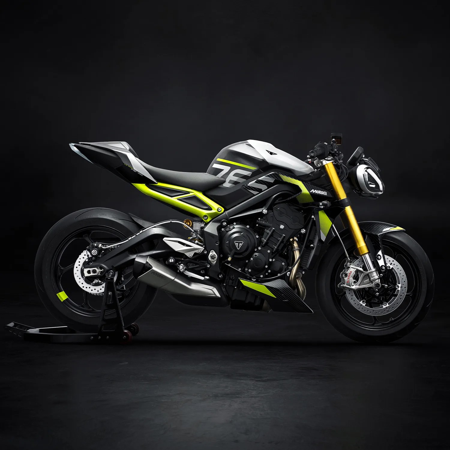 Black and neon yellow sport motorcycle with gold front forks on a black stand against a dark background.