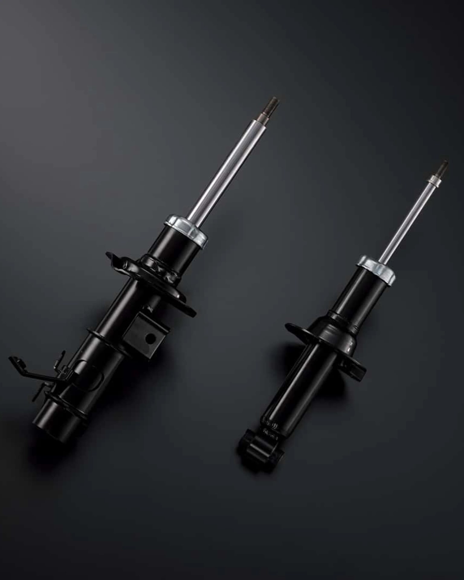 Two black automotive shock absorbers with silver piston rods on a dark surface.