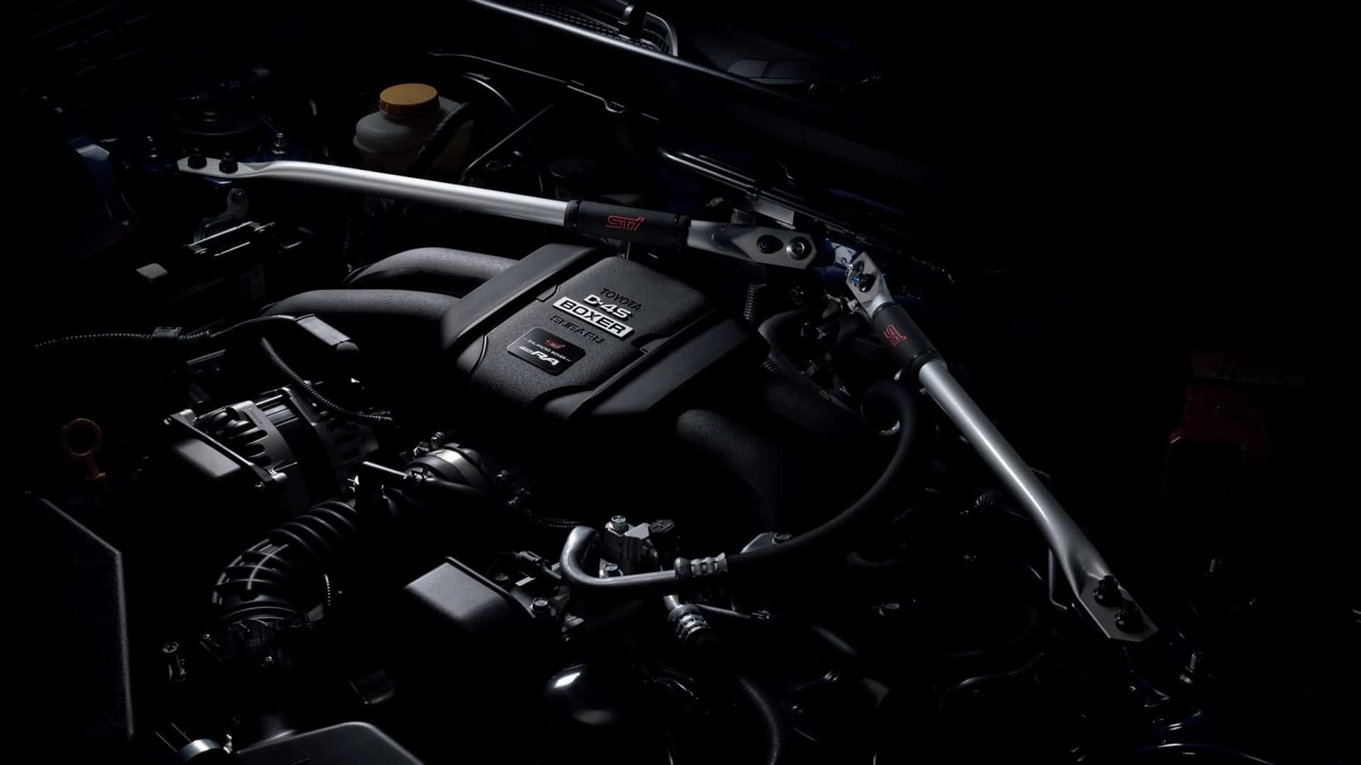 Toyota D-4S Boxer engine with STI-branded silver strut bar installed in a dark engine bay.