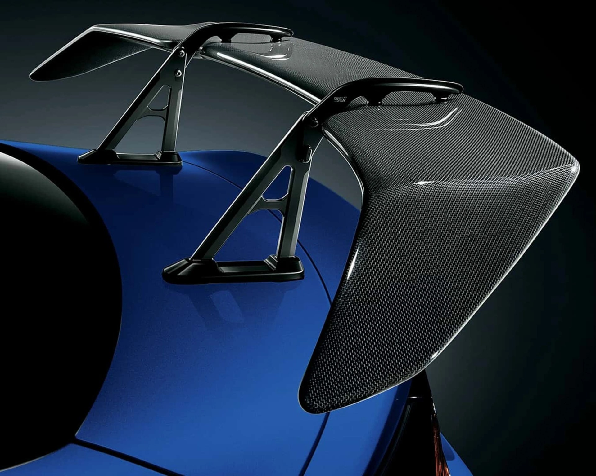 Glossy carbon fiber rear spoiler mounted on a blue sports car.