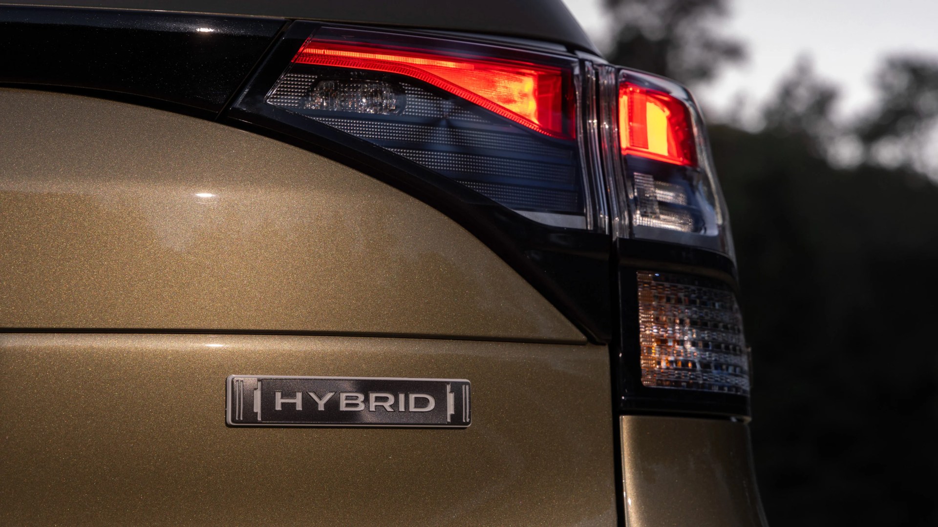 Close-up of a gold car's rear with a "HYBRID" badge and illuminated red tail light.