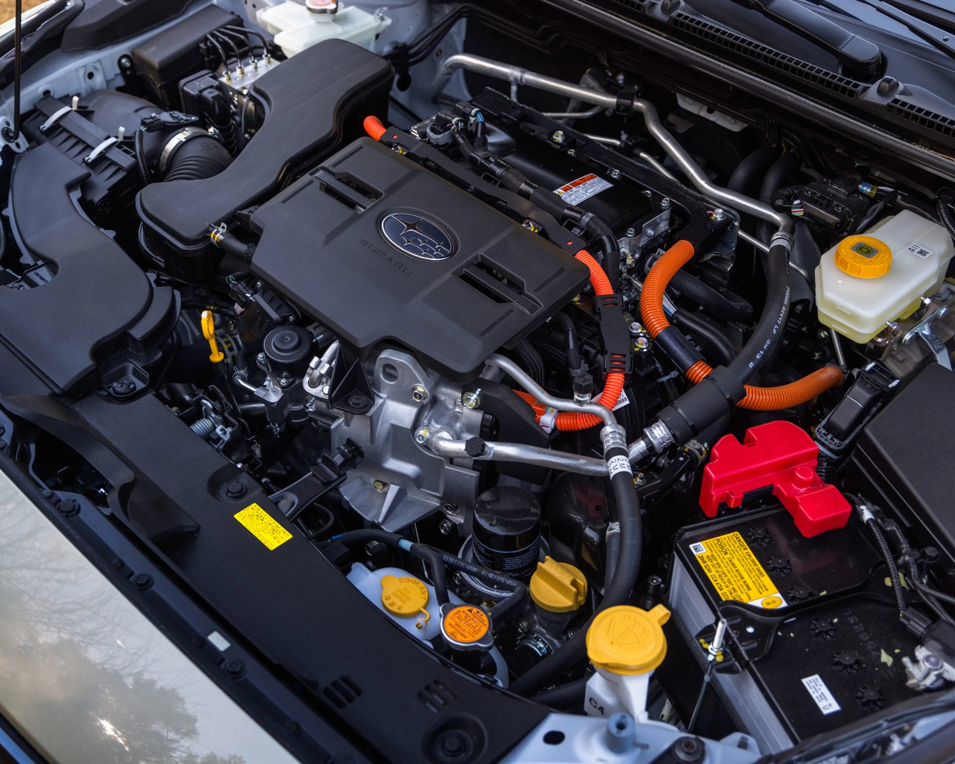Subaru car engine bay with black engine cover, orange cables, and yellow fluid caps.