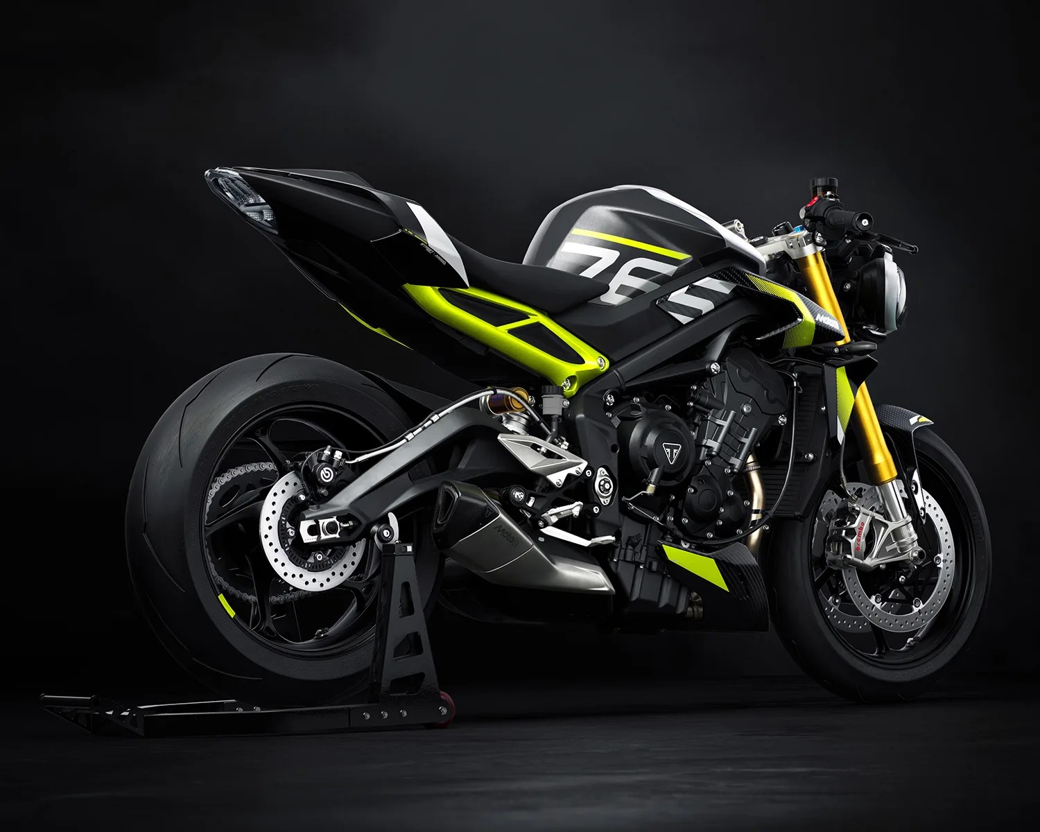 Black and neon yellow Triumph motorcycle with gold front forks on a black stand against a dark background.