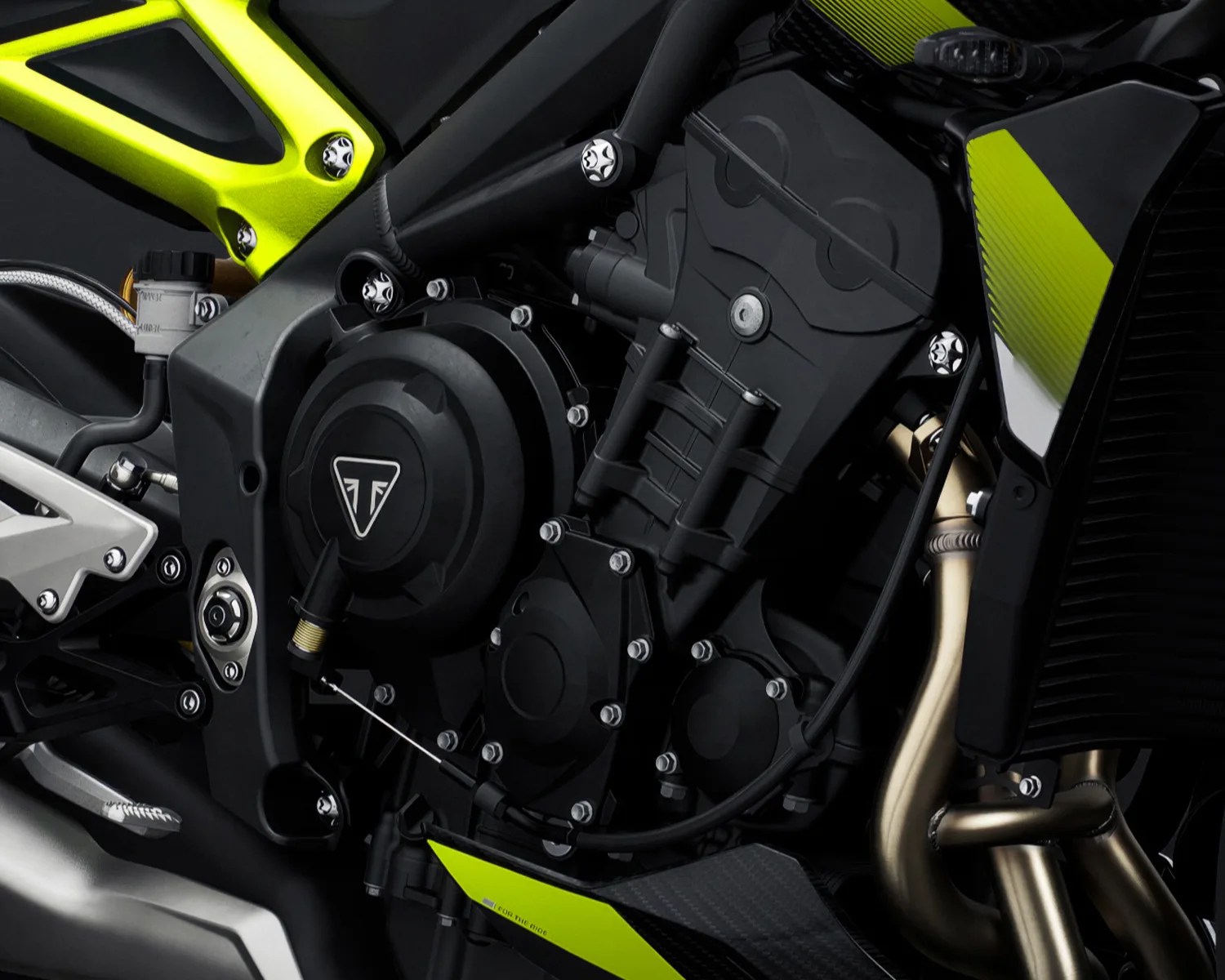 Close-up of a black motorcycle engine with neon yellow frame accents and metallic exhaust pipes.